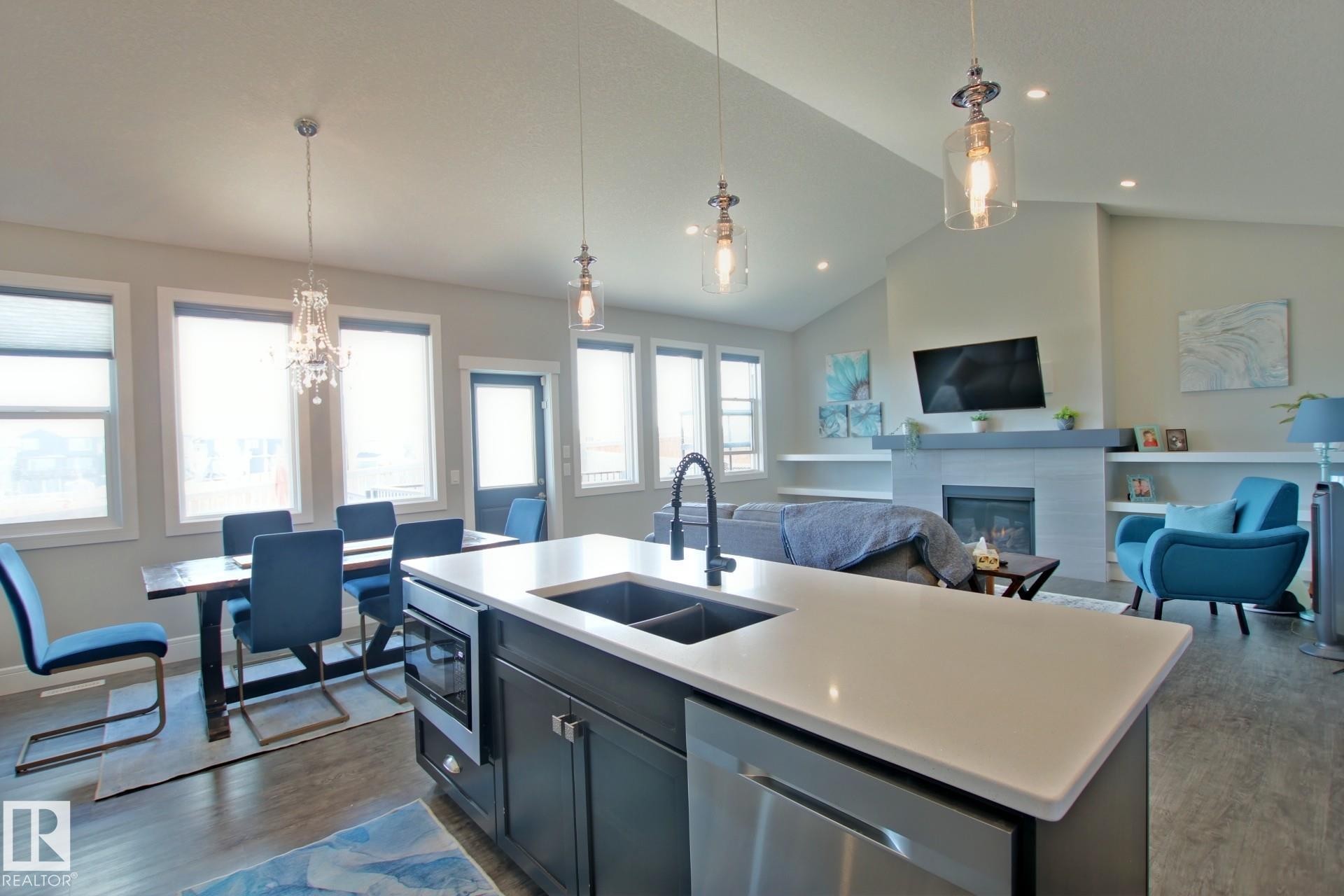 Open-concept living area featuring a kitchen island with dual sinks and built-in microwave, wood-finish flooring, vaulted ceilings, and a fireplace with integrated shelving - 9711 223 Street, Edmonton, AB
