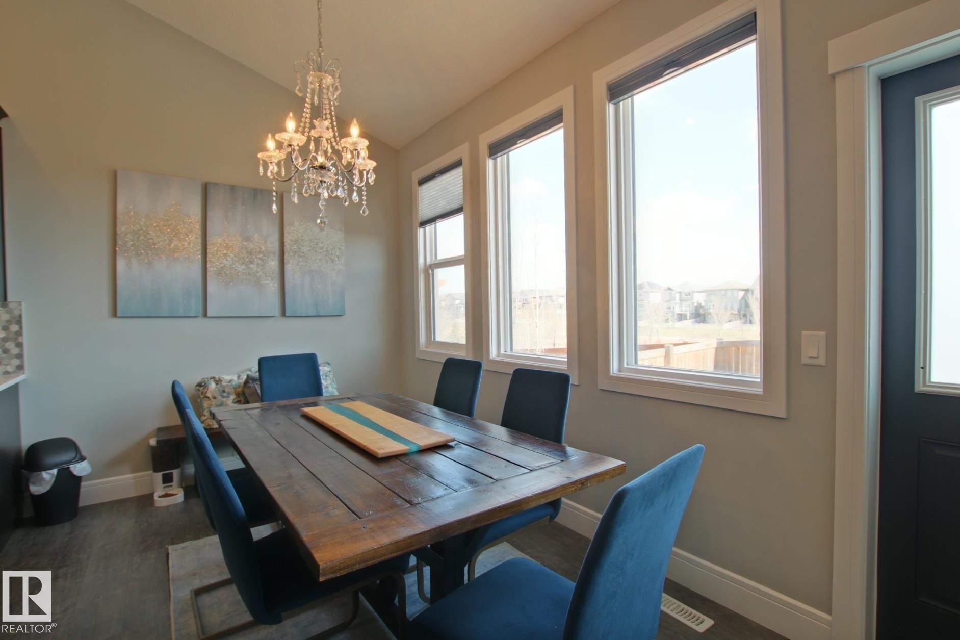 Dining area featuring a crystal chandelier, wood-finish flooring, and multiple windows - 9711 223 Street, Edmonton, AB