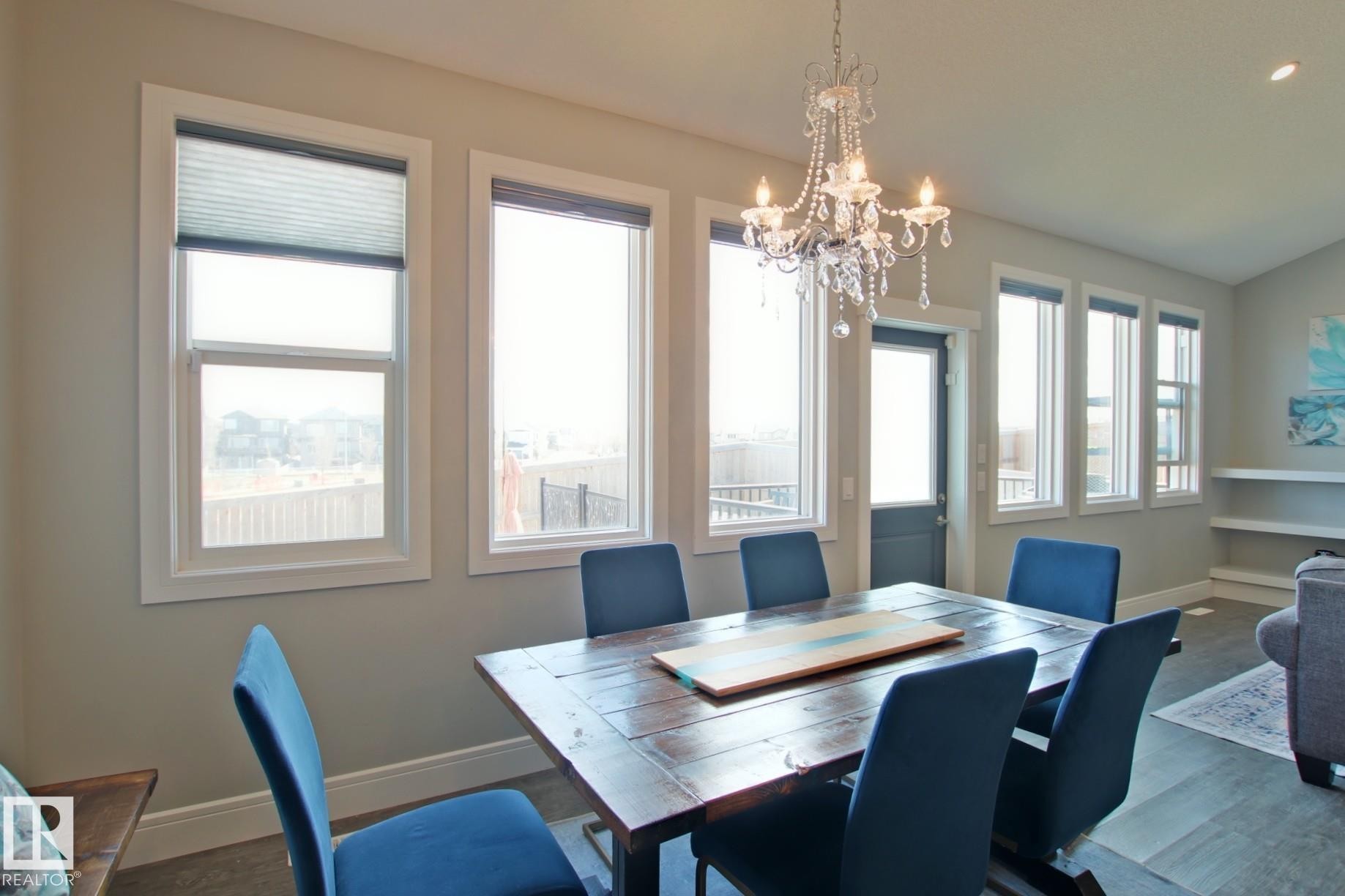 Dining area featuring a chandelier, multiple windows with blinds, and a rear exterior door - 9711 223 Street, Edmonton, AB
