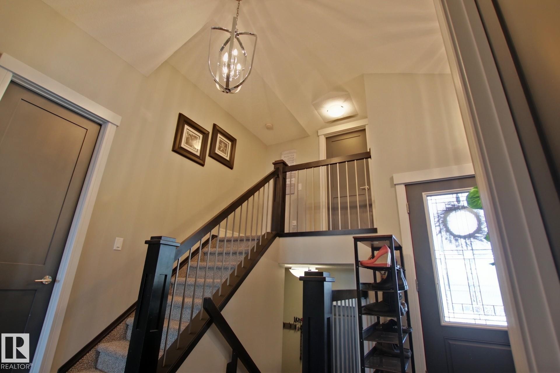 Two-story foyer featuring a carpeted staircase with dark wood newel posts and handrail, metal balusters, and a decorative overhead light fixture - 9711 223 Street, Edmonton, AB