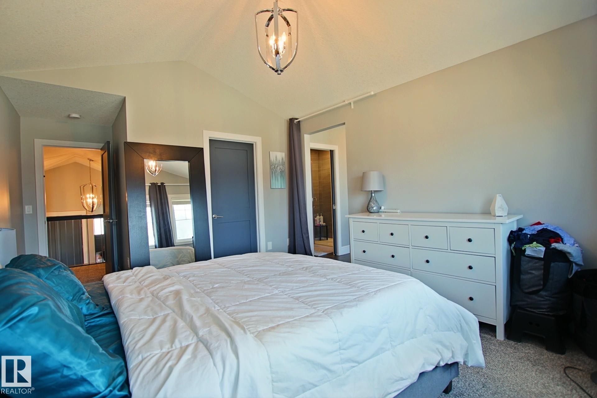 Vaulted ceiling bedroom with a modern overhead light fixture, light gray walls, dark gray door, and soft gray carpeting - 9711 223 Street, Edmonton, AB