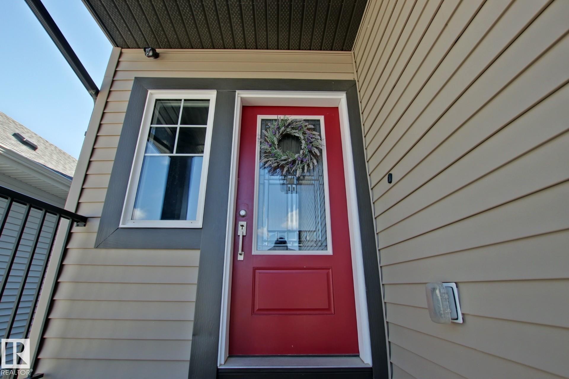 Vibrant red entry door with glass paneling and a white frame, complemented by light beige siding - 9711 223 Street, Edmonton, AB