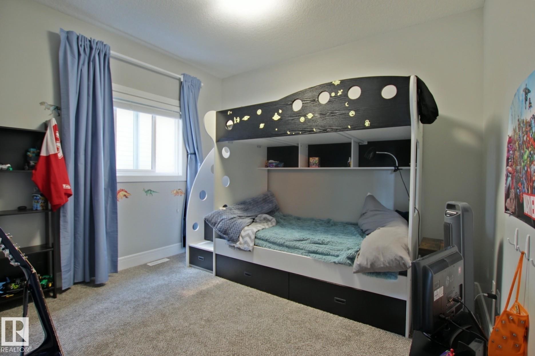 Bedroom featuring wall-to-wall carpeting, a double window with blinds and curtain rods, and a multi-level bunk bed with integrated shelving and drawer storage - 9711 223 Street, Edmonton, AB