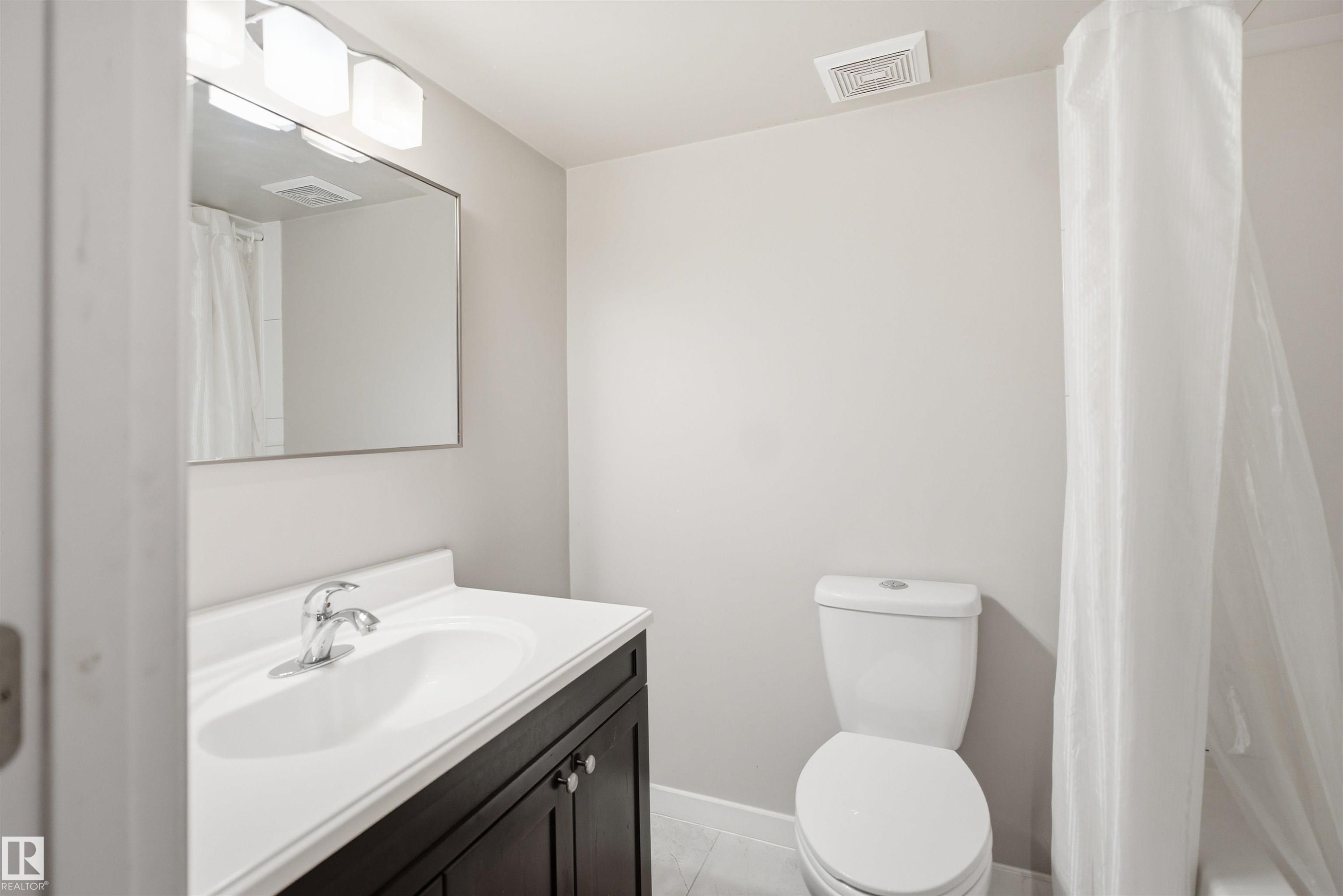 Contemporary bathroom featuring a dark wood-finish vanity with a white countertop and integrated sink, a polished chrome faucet, and a rectangular wall mirror - 7323 24 Ave, Edmonton, AB - Indoor Photo Showing Other Room