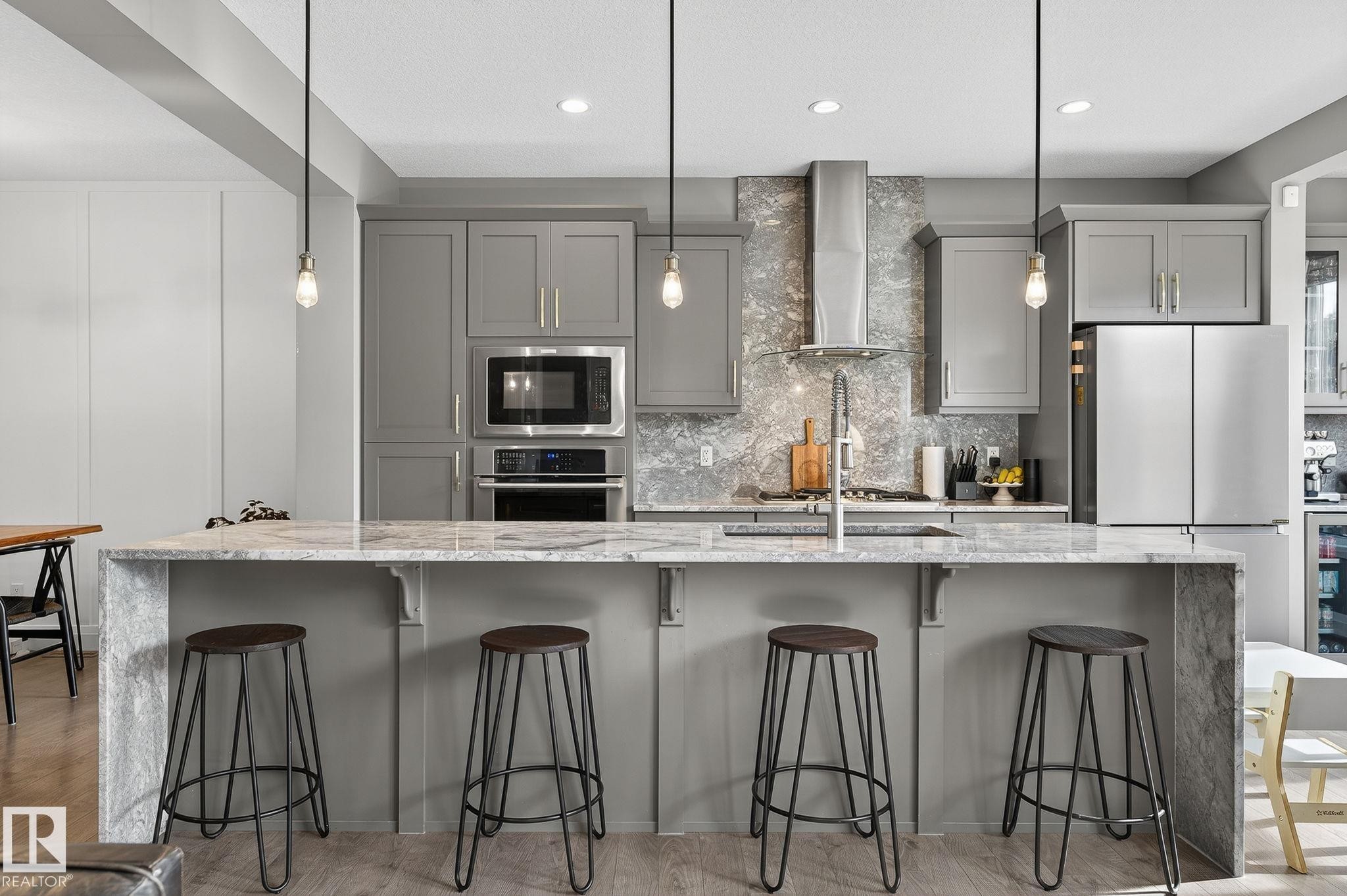 Modern kitchen featuring a waterfall island with a stone-finish countertop, gray cabinetry, stainless steel appliances, and pendant lighting - 1737 Dumont Crescent, Edmonton, AB - Indoor Photo Showing Kitchen With Upgraded Kitchen