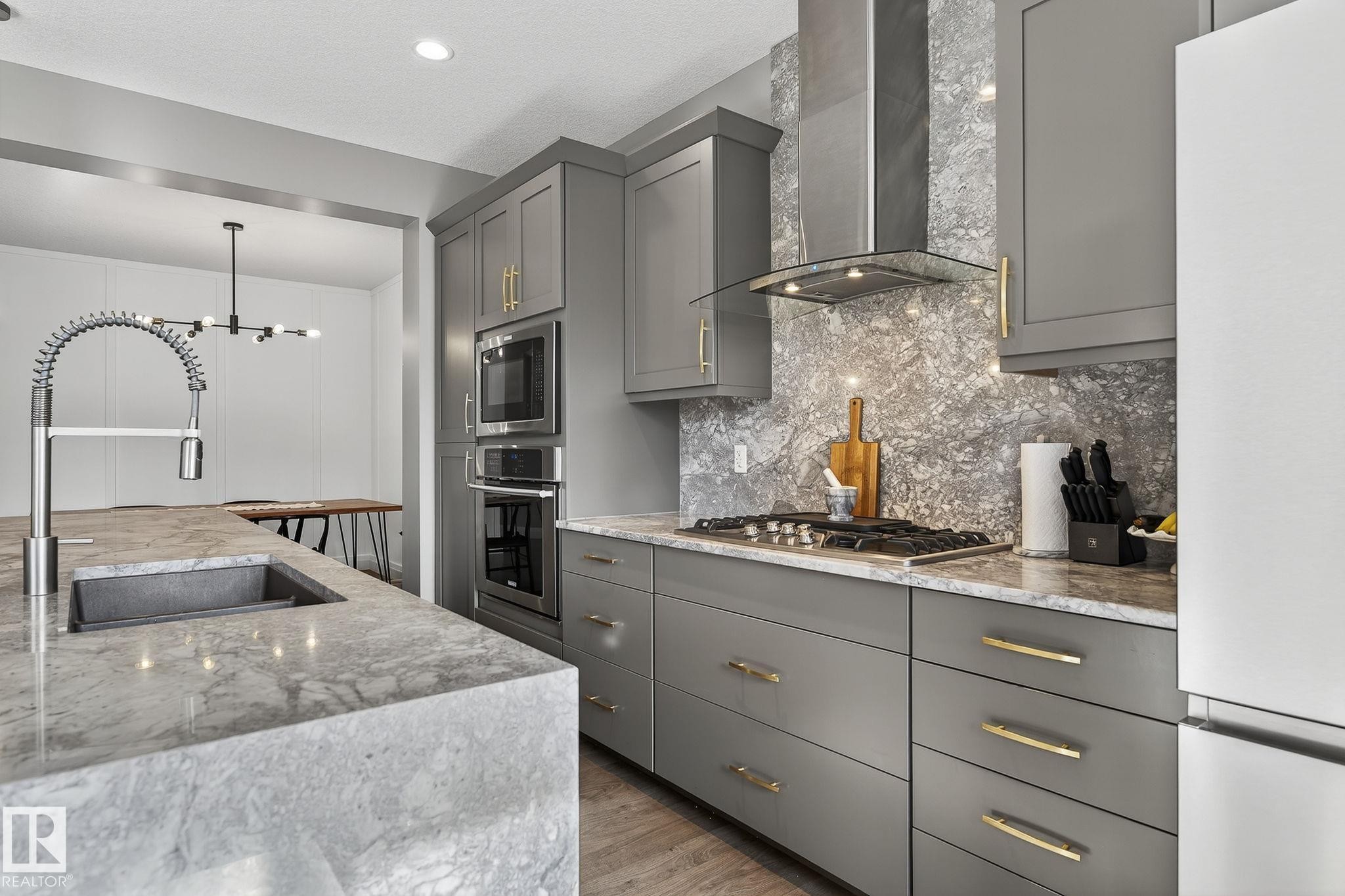 Kitchen featuring grey cabinetry with gold-tone hardware, a stainless steel gas range, built-in microwave and oven, an oversized island with a built-in sink, and a modern industrial-style faucet - 1737 Dumont Crescent, Edmonton, AB - Indoor Photo Showing Kitchen With Upgraded Kitchen