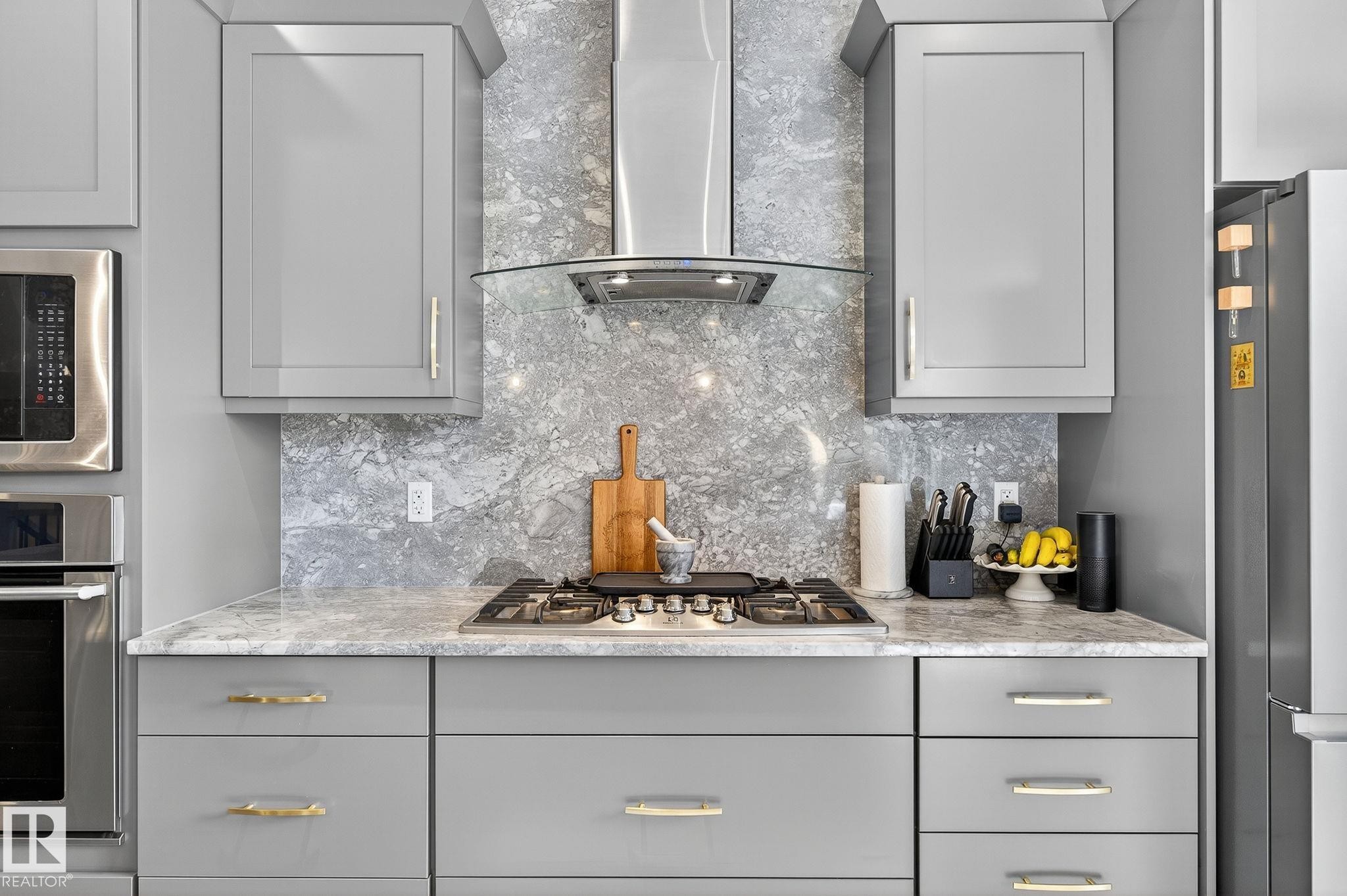 Modern kitchen featuring light gray cabinetry with gold-tone hardware, a stainless steel gas range, and a coordinating range hood - 1737 Dumont Crescent, Edmonton, AB - Indoor Photo Showing Kitchen With Upgraded Kitchen