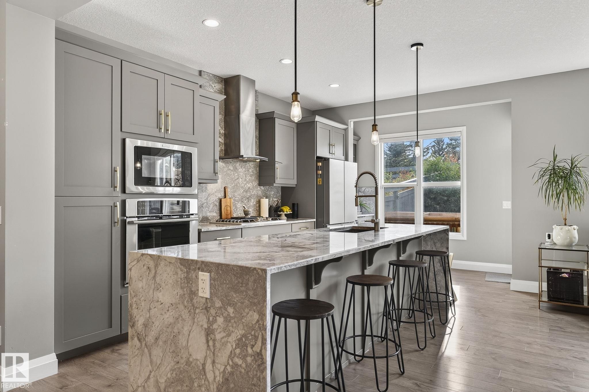 Contemporary kitchen featuring an oversized island with waterfall countertop, pendant lighting, stainless steel appliances, and grey cabinetry - 1737 Dumont Crescent, Edmonton, AB - Indoor Photo Showing Kitchen With Upgraded Kitchen