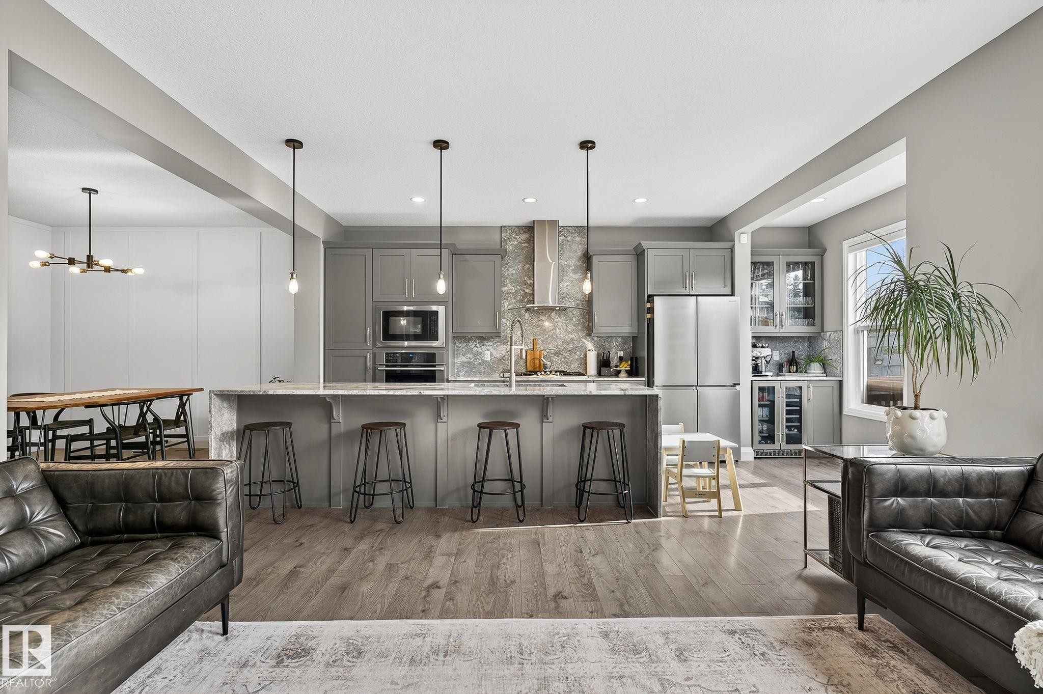 Open-concept kitchen featuring an oversized island with seating, pendant lighting, stainless steel appliances, wood-finish flooring, and gray cabinetry with a complementary tiled backsplash - 1737 Dumont Crescent, Edmonton, AB - Indoor