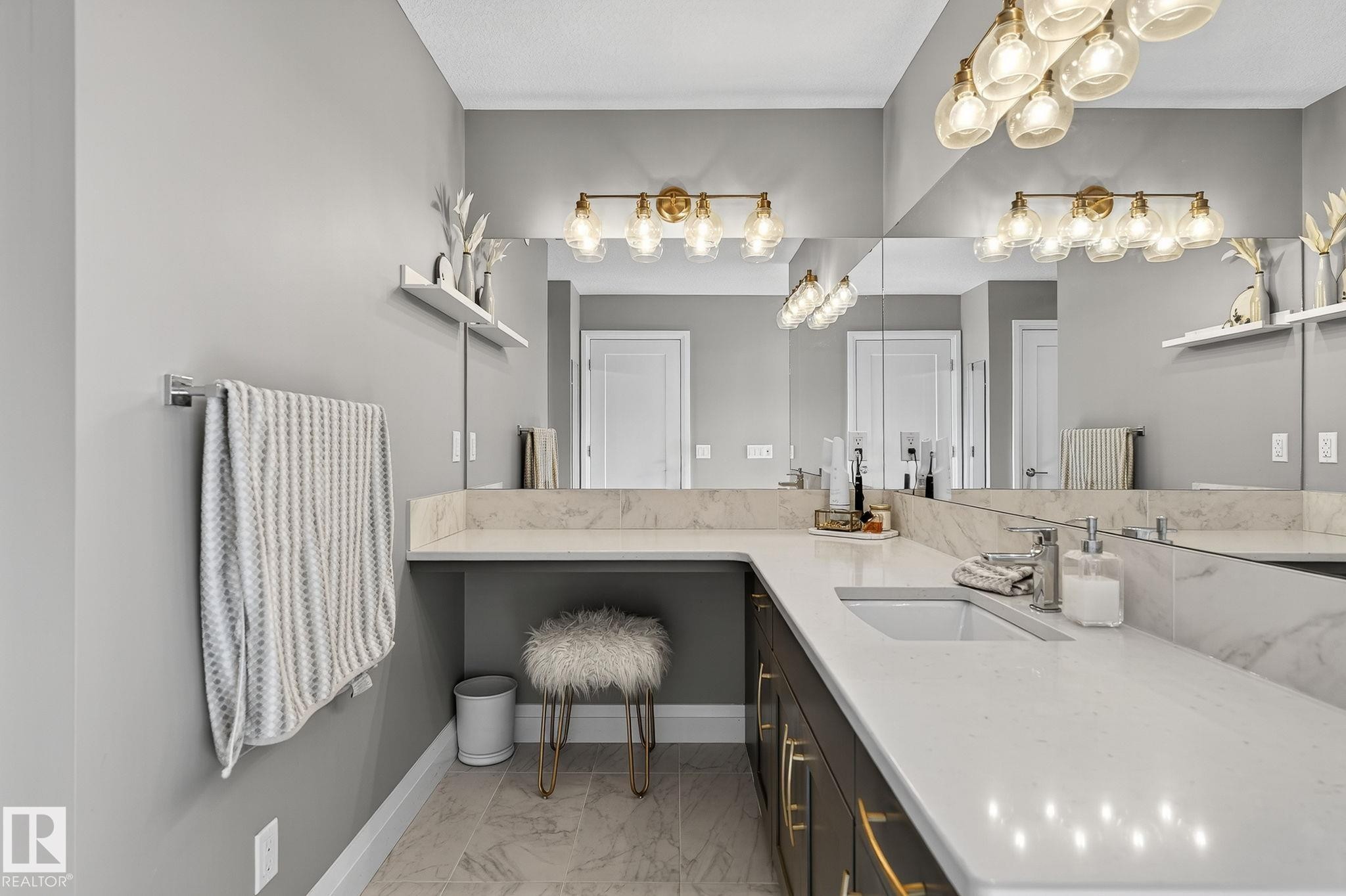 Bathroom vanity featuring an integrated rectangular sink, light-toned countertop, dark wood-finish cabinetry with gold-toned hardware, full-width mirror, and a multi-bulb light fixture - 1737 Dumont Crescent, Edmonton, AB - Indoor Photo Showing Other Room