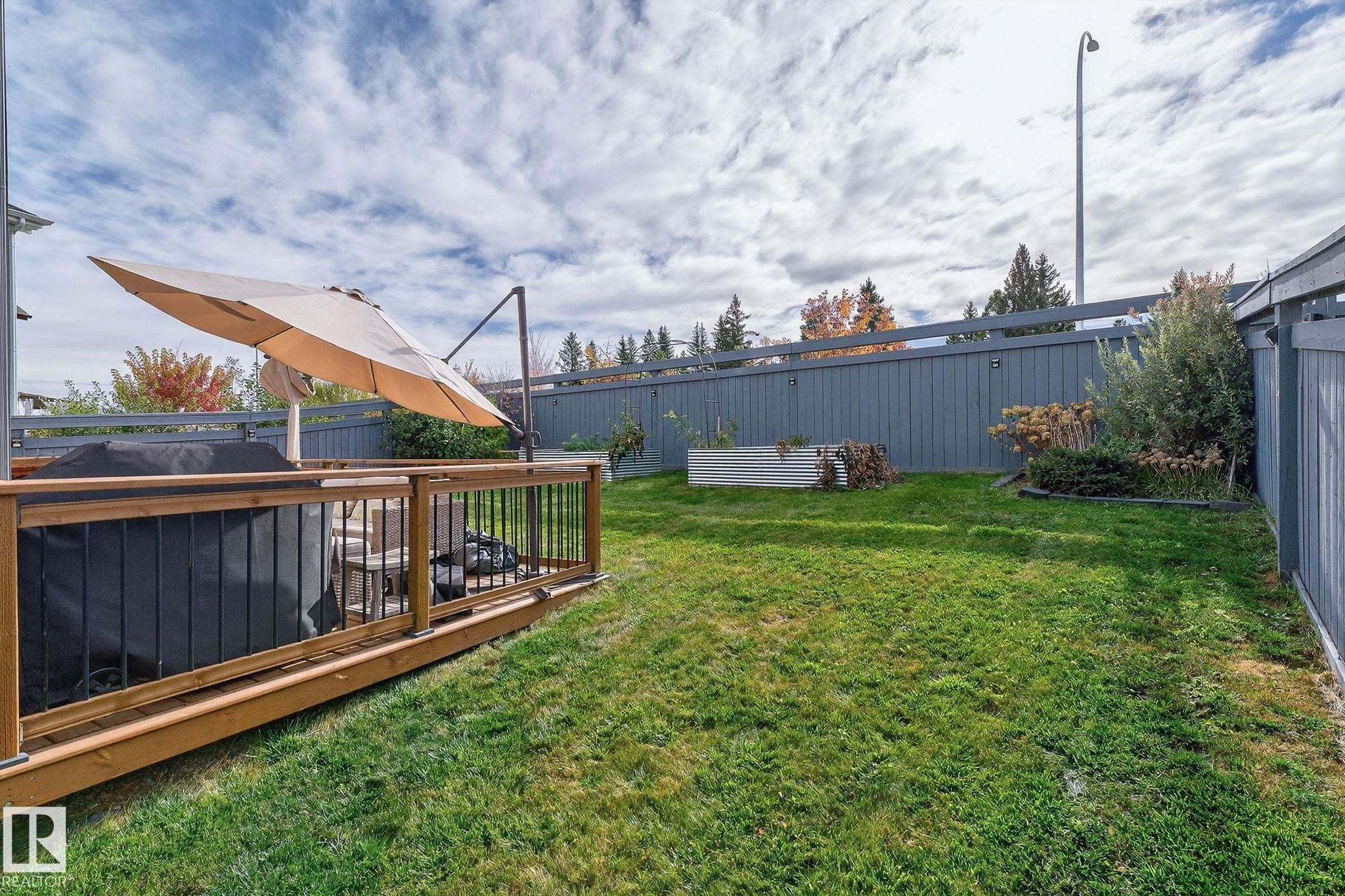 Expansive backyard featuring a wood deck with wood railing, a level lawn area, and perimeter fencing - 1737 Dumont Crescent, Edmonton, AB - Outdoor With Deck Patio Veranda