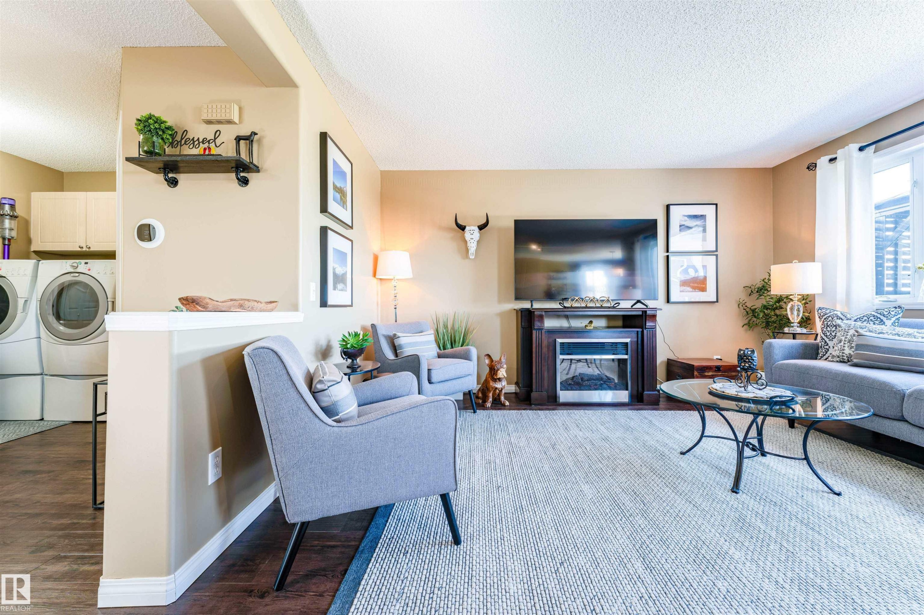 Open-concept living area featuring a built-in electric fireplace with a dark wood mantel, light tan walls, and a window with white curtains - 847 Blacklock Way, Edmonton, AB - Indoor Photo Showing Living Room With Fireplace