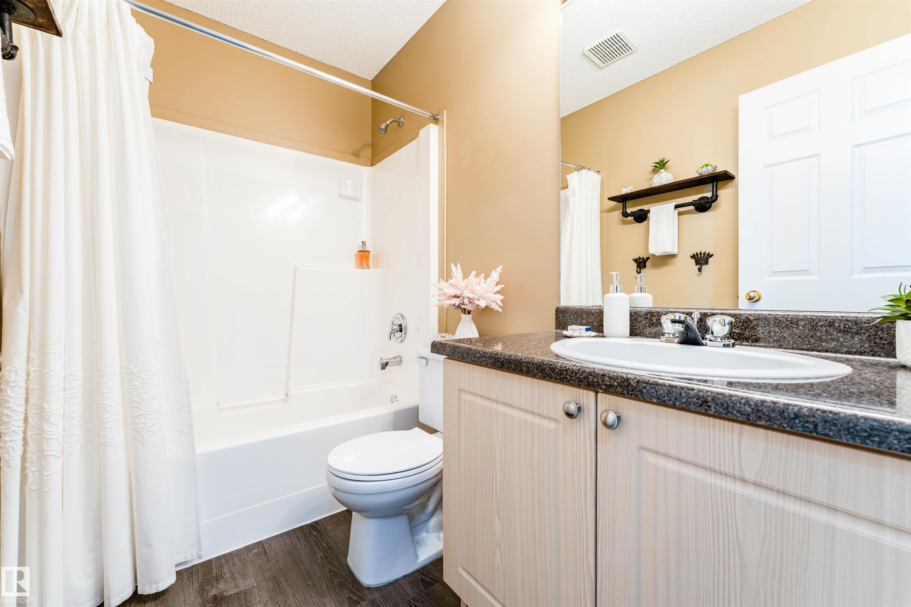 Bathroom featuring a white tub/shower combination, white toilet, single vanity with integrated sink, dark speckled countertop, and wood-finish flooring - 847 Blacklock Way, Edmonton, AB - Indoor Photo Showing Bathroom