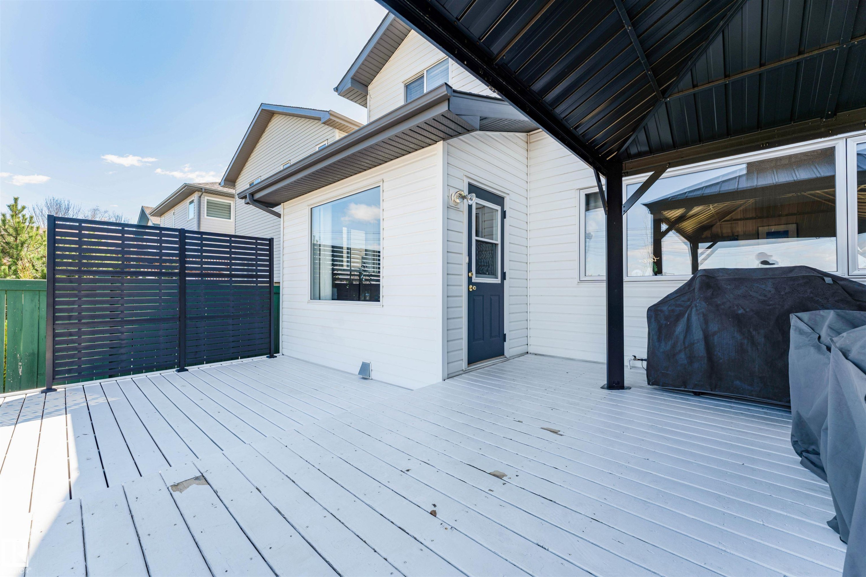 Spacious outdoor deck featuring light-colored decking, a dark blue exterior door, and a black privacy screen - 847 Blacklock Way, Edmonton, AB - Outdoor With Deck Patio Veranda With Exterior