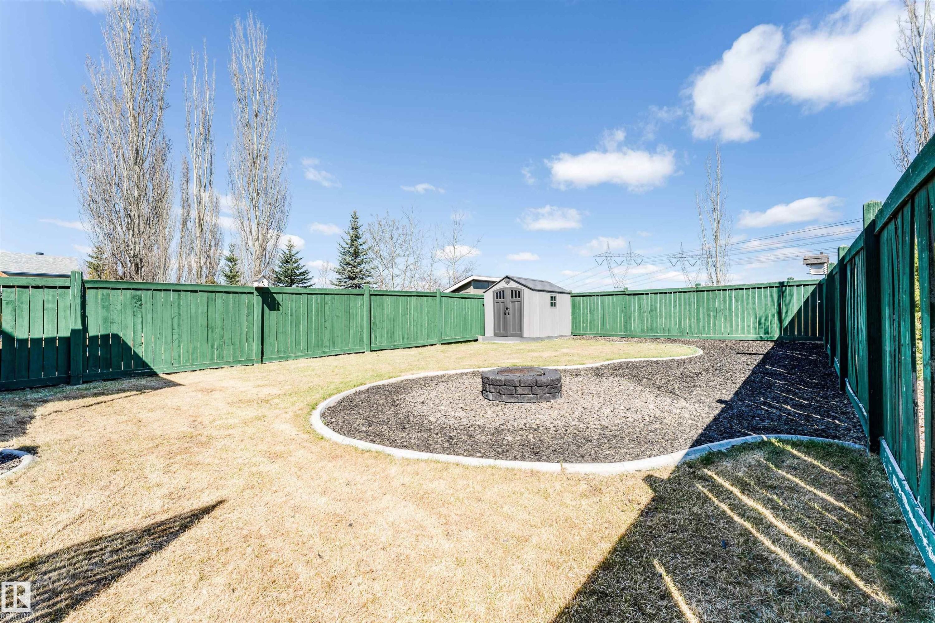 Spacious backyard featuring a green privacy fence, a detached storage shed, a defined bark mulch area with a built-in fire pit, and an expansive lawn - 847 Blacklock Way, Edmonton, AB - Outdoor