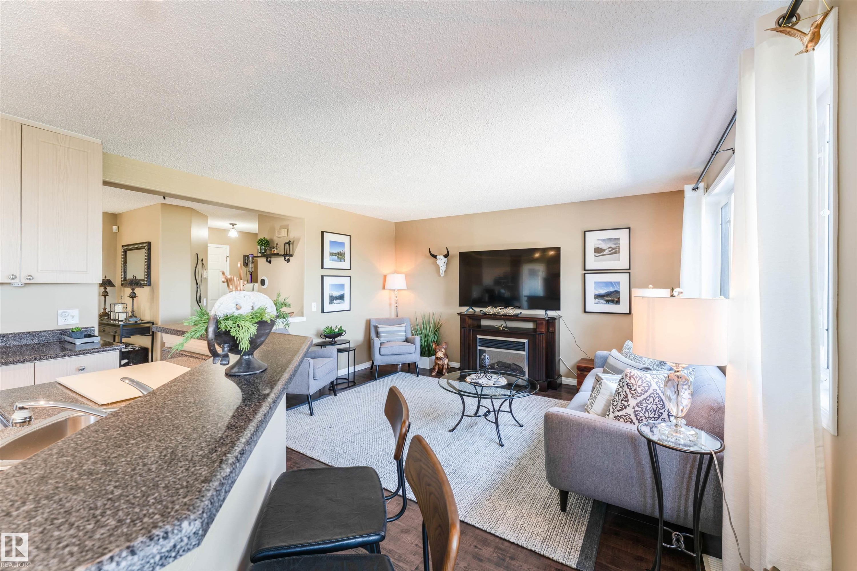Open-concept living space featuring wood-finish flooring, a built-in electric fireplace, a breakfast bar with stone-look countertops, and recessed lighting - 847 Blacklock Way, Edmonton, AB - Indoor Photo Showing Living Room