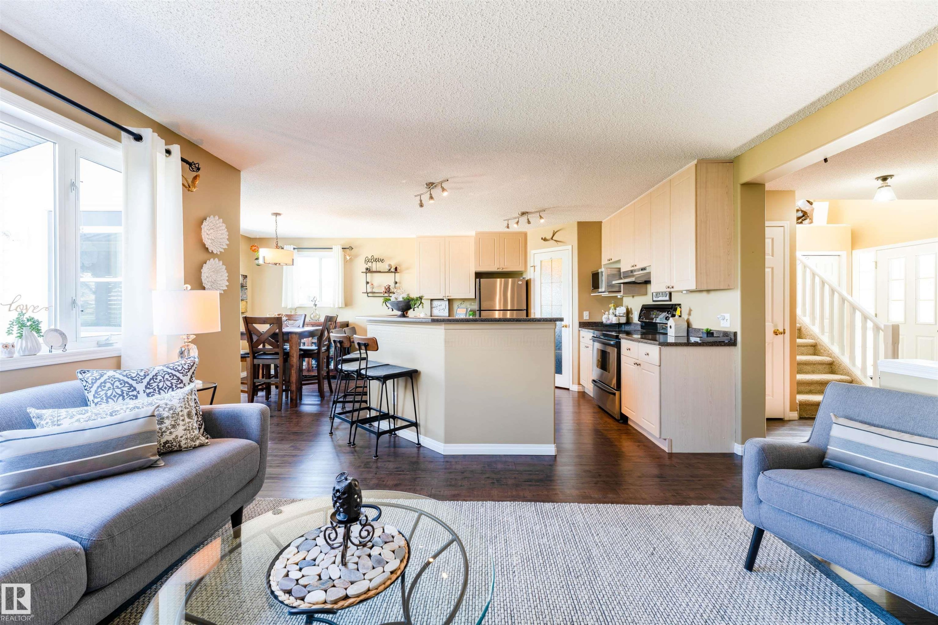 Spacious open-concept living area featuring wood-finish flooring, a kitchen island with seating, stainless steel appliances, and ample natural light from large windows - 847 Blacklock Way, Edmonton, AB - Indoor Photo Showing Living Room