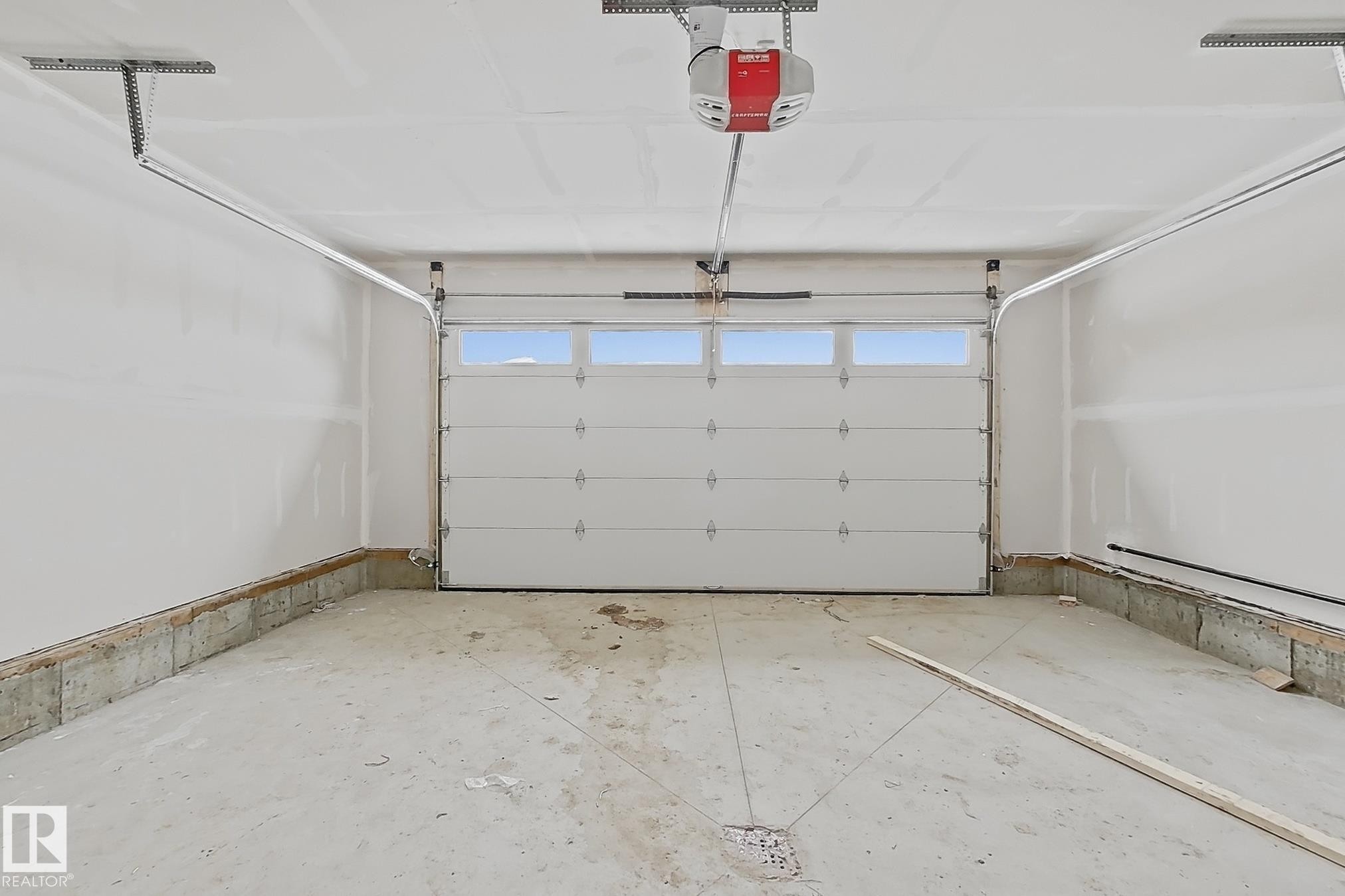 The property includes a spacious garage with a white overhead door featuring upper window panels, and a ceiling-mounted garage door opener - 17 Trill Point(E), Spruce Grove, AB - Indoor Photo Showing Garage