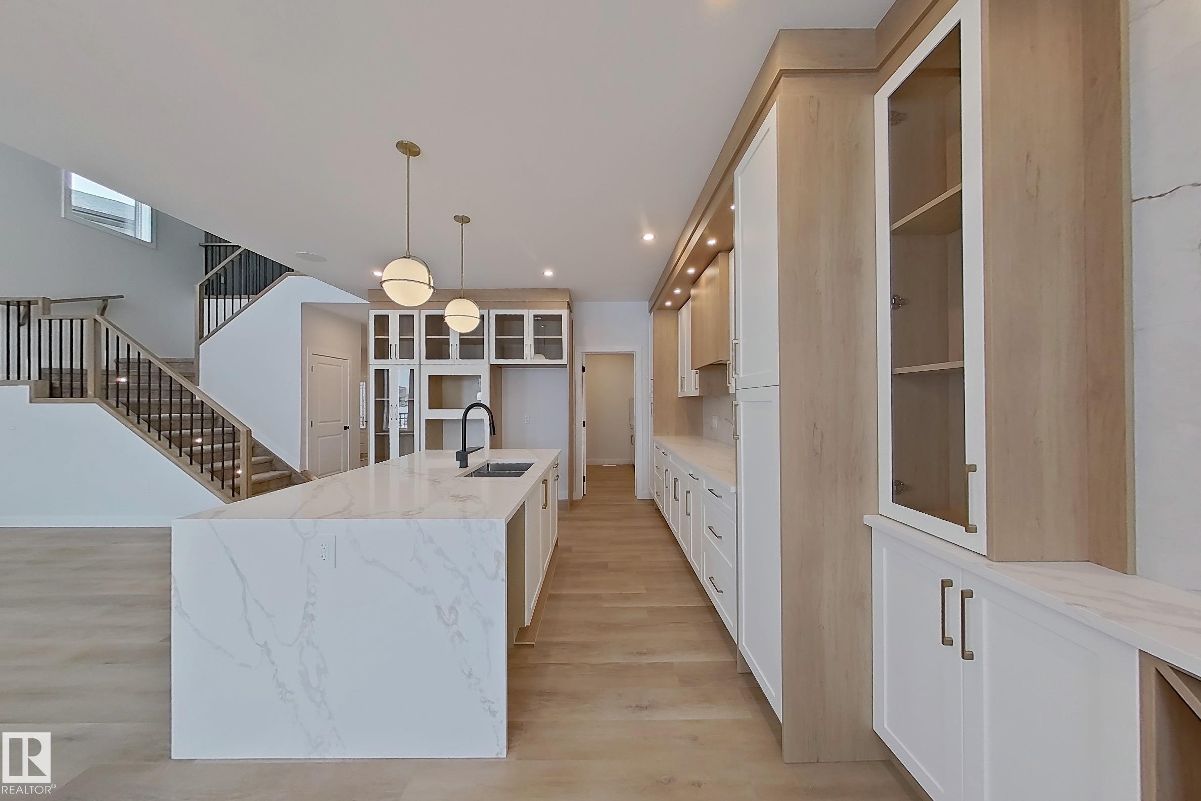 The kitchen features an island with a waterfall countertop, a black kitchen faucet, and pendant lighting - 17 Trill Point(E), Spruce Grove, AB - Indoor
