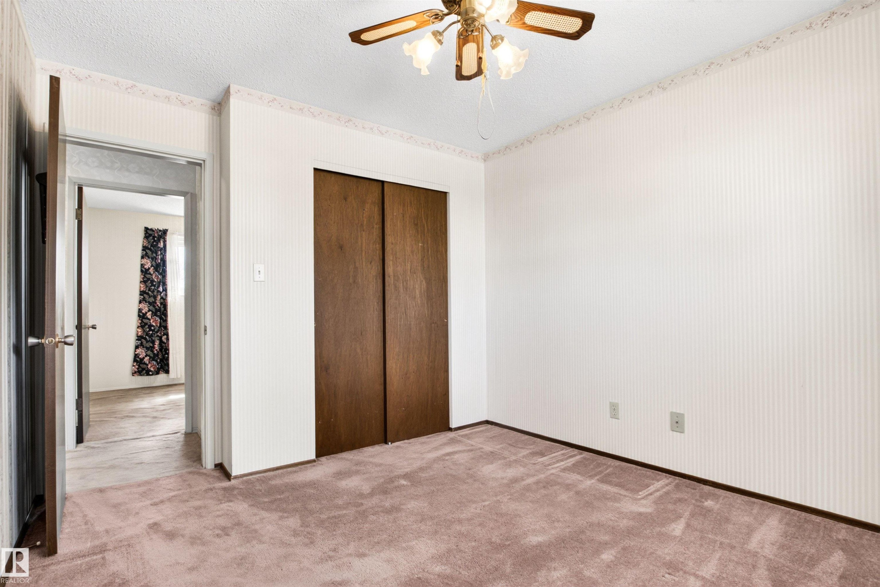 Carpeted room featuring a ceiling fan with light fixture, white patterned wallpaper, and a dark wood bifold closet door - 29 Bristow Crescent, Spruce Grove, AB - Indoor Photo Showing Other Room