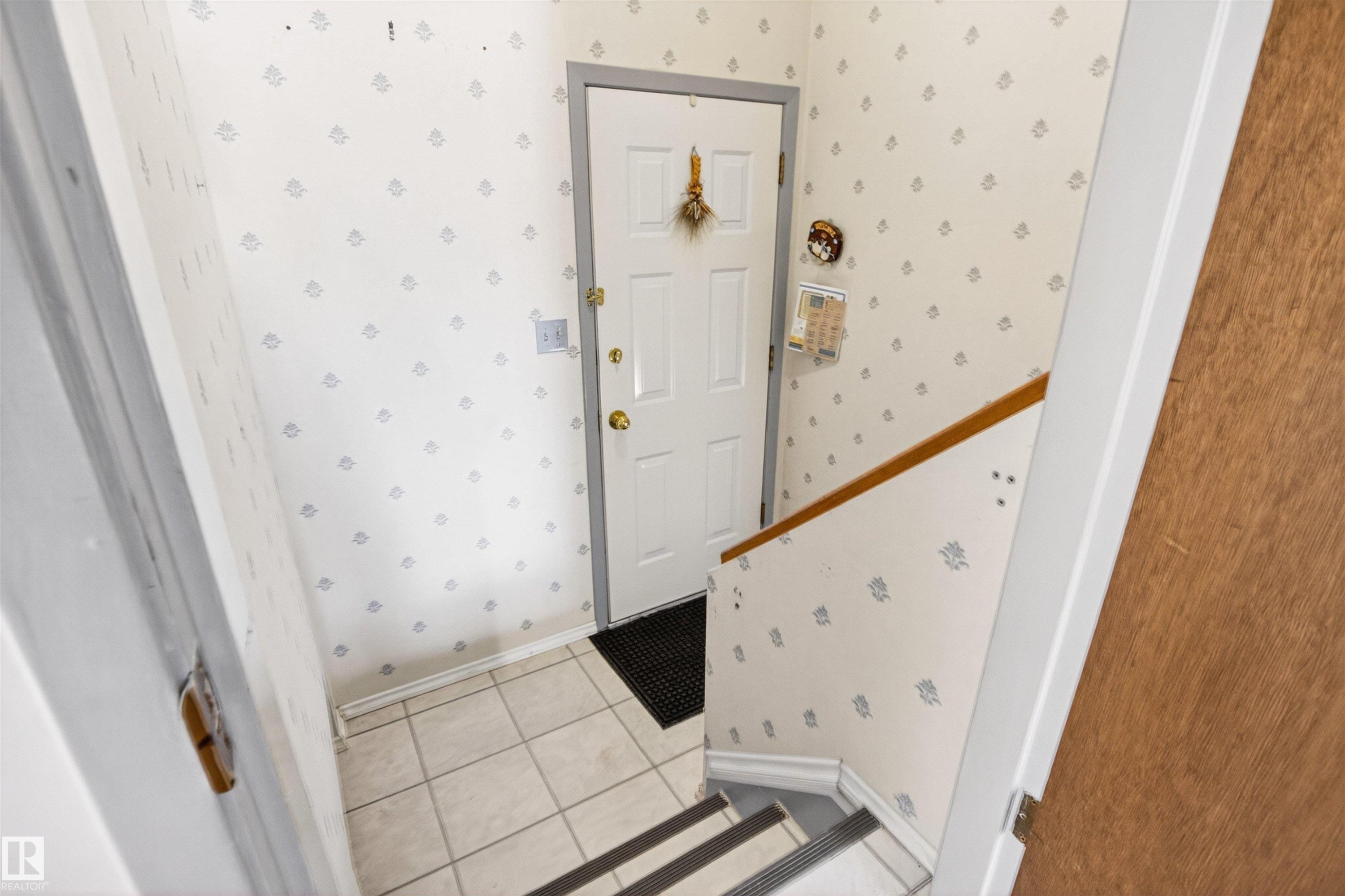 Entryway featuring a paneled door with brass hardware, tile flooring, and a wooden handrail - 29 Bristow Crescent, Spruce Grove, AB - Indoor Photo Showing Other Room