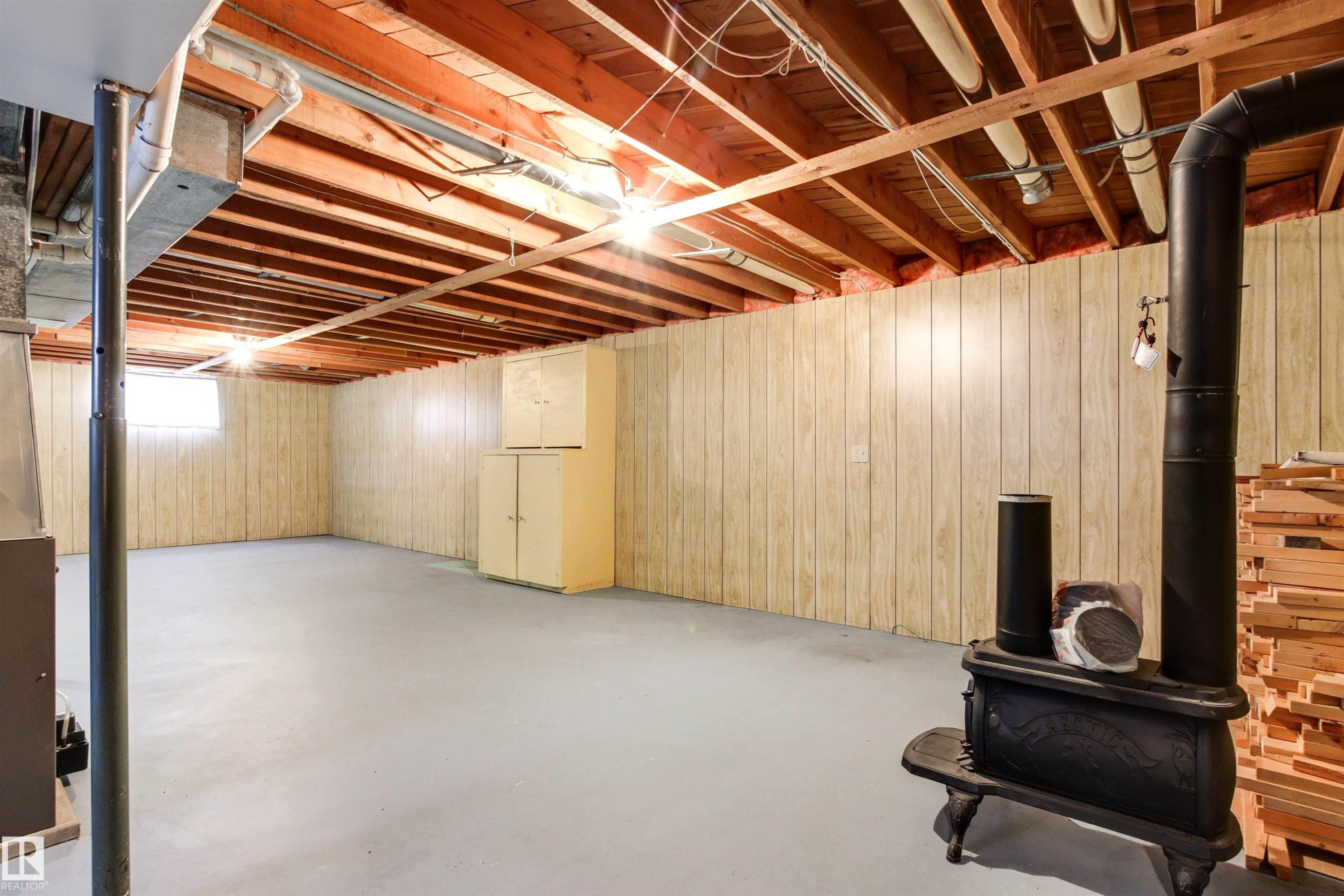 Spacious basement area featuring exposed wooden ceiling joists, light-colored paneling, and a cast iron stove - 29 Bristow Crescent, Spruce Grove, AB - Indoor Photo Showing Basement