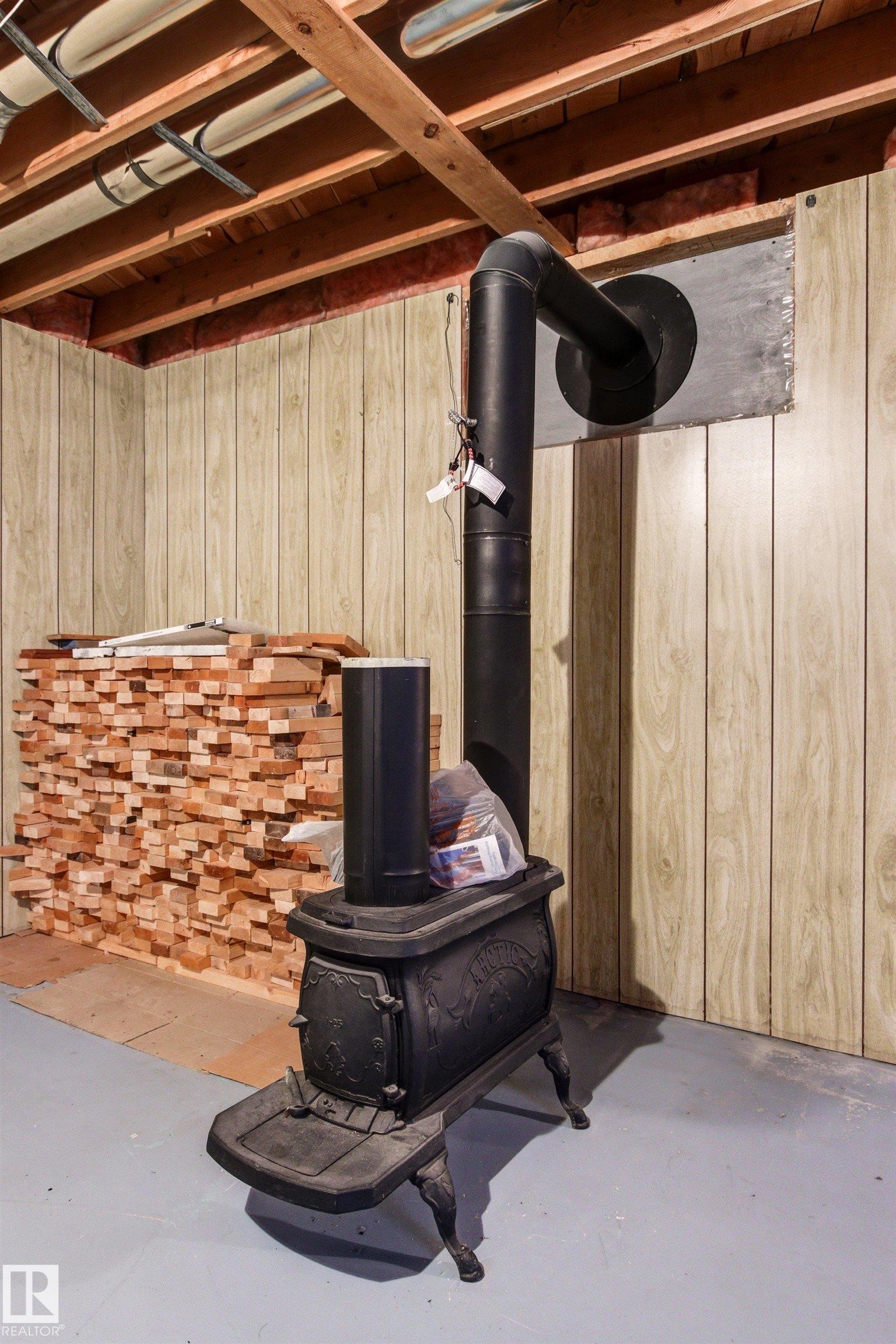 Cast iron wood-burning stove with a black stovepipe, installed on a gray concrete floor - 29 Bristow Crescent, Spruce Grove, AB - Indoor Photo Showing Basement