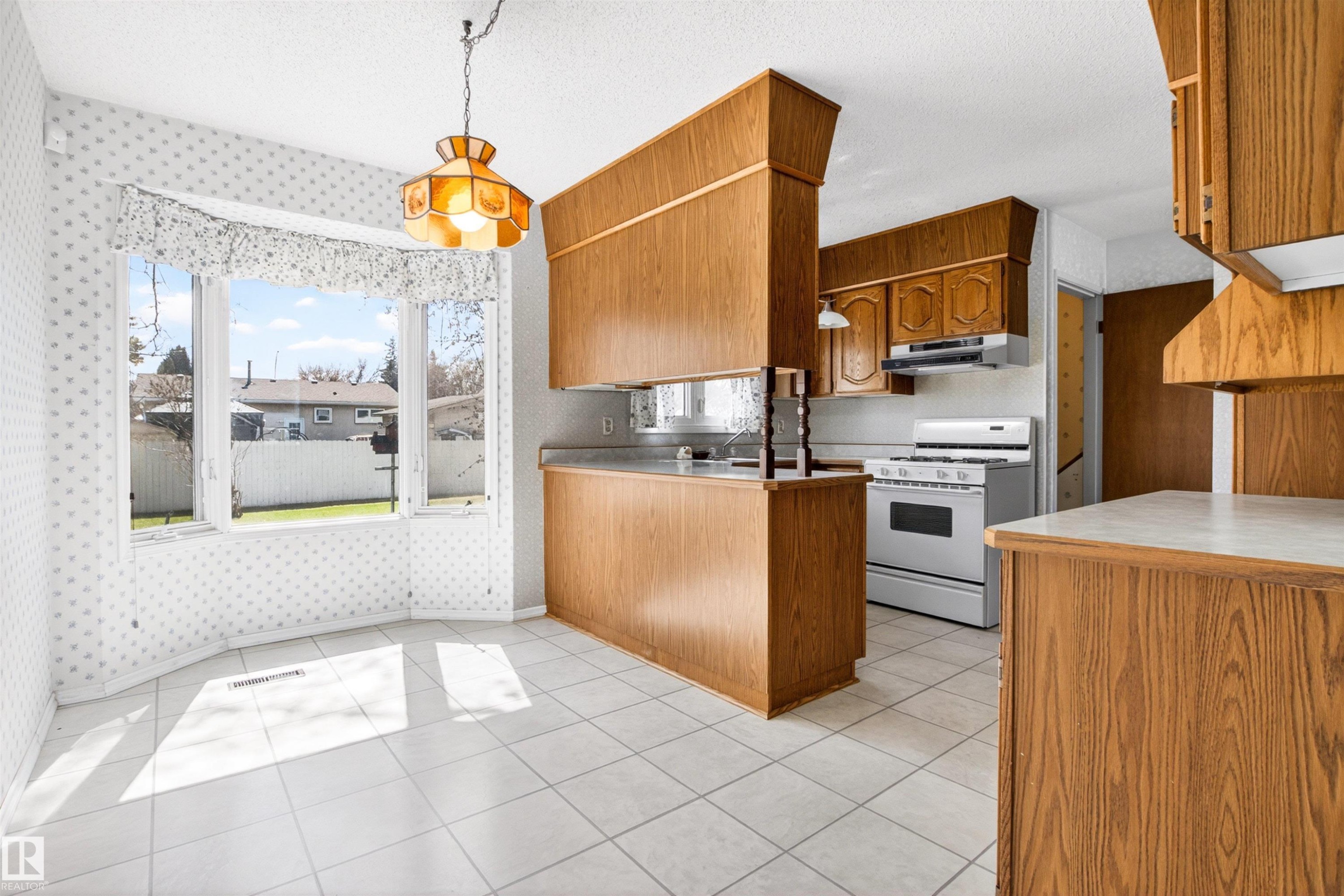 Bright kitchen and dining area featuring wood-finish cabinetry, a white tile floor, and a bay window - 29 Bristow Crescent, Spruce Grove, AB - Indoor Photo Showing Kitchen