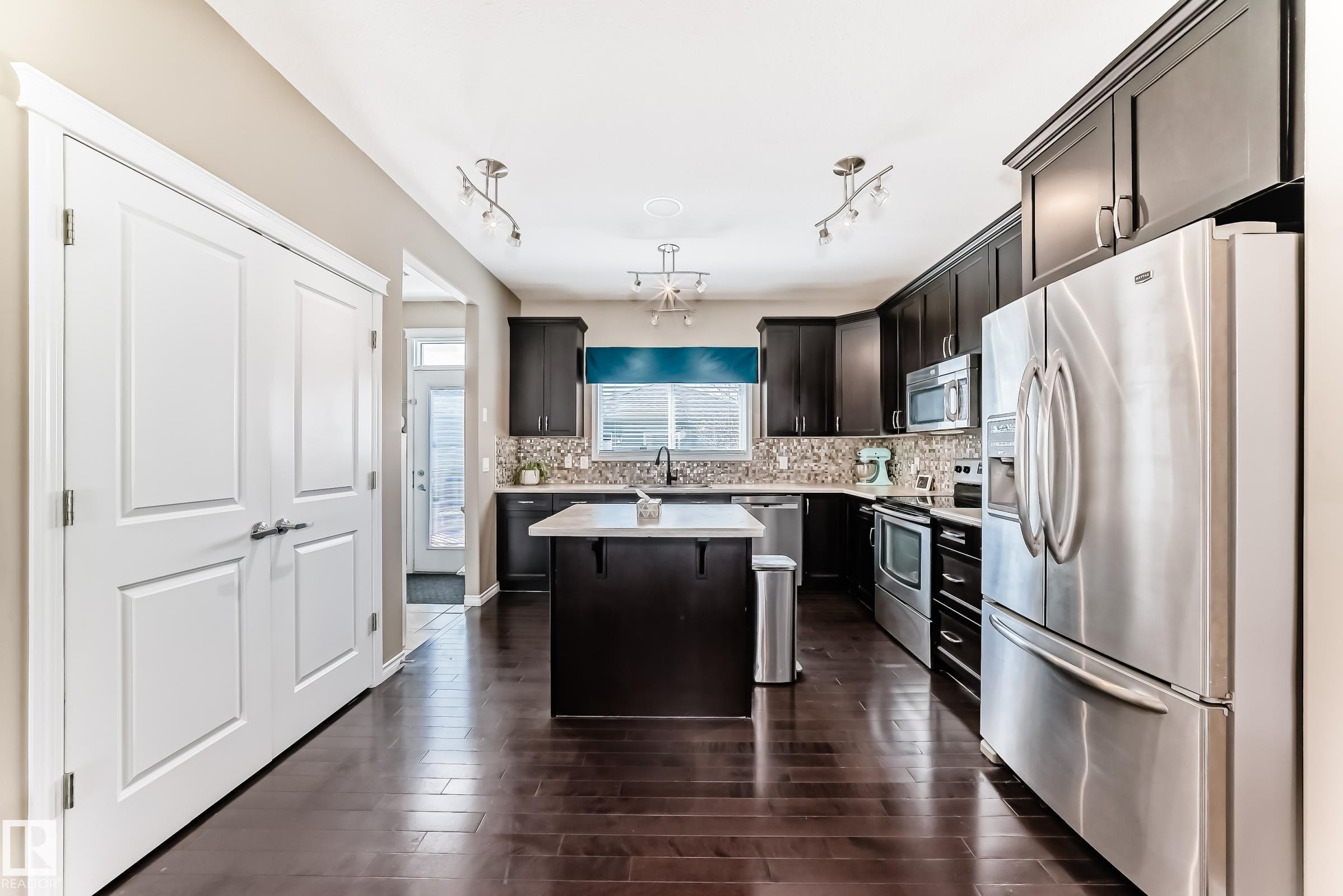 Kitchen featuring dark wood-finish cabinetry, stainless steel appliances, a center island with a light-toned countertop, and dark wood-finish flooring - 5020 Orchards Gate, Edmonton, AB - Indoor Photo Showing Kitchen With Stainless Steel Kitchen With Upgraded Kitchen