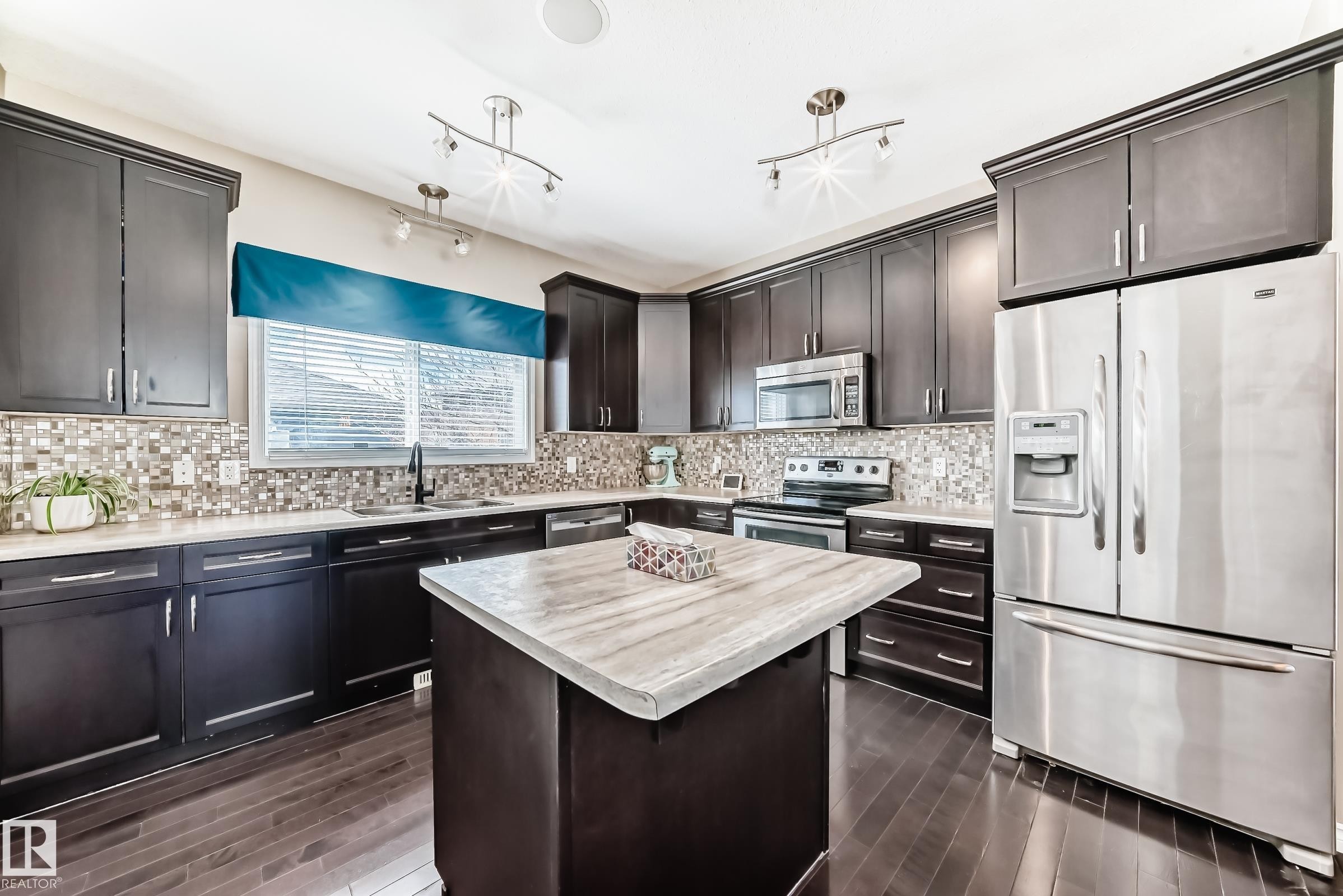 Expansive kitchen featuring dark wood cabinetry, a mosaic tile backsplash, and stainless steel appliances - 5020 Orchards Gate, Edmonton, AB - Indoor Photo Showing Kitchen With Stainless Steel Kitchen With Upgraded Kitchen