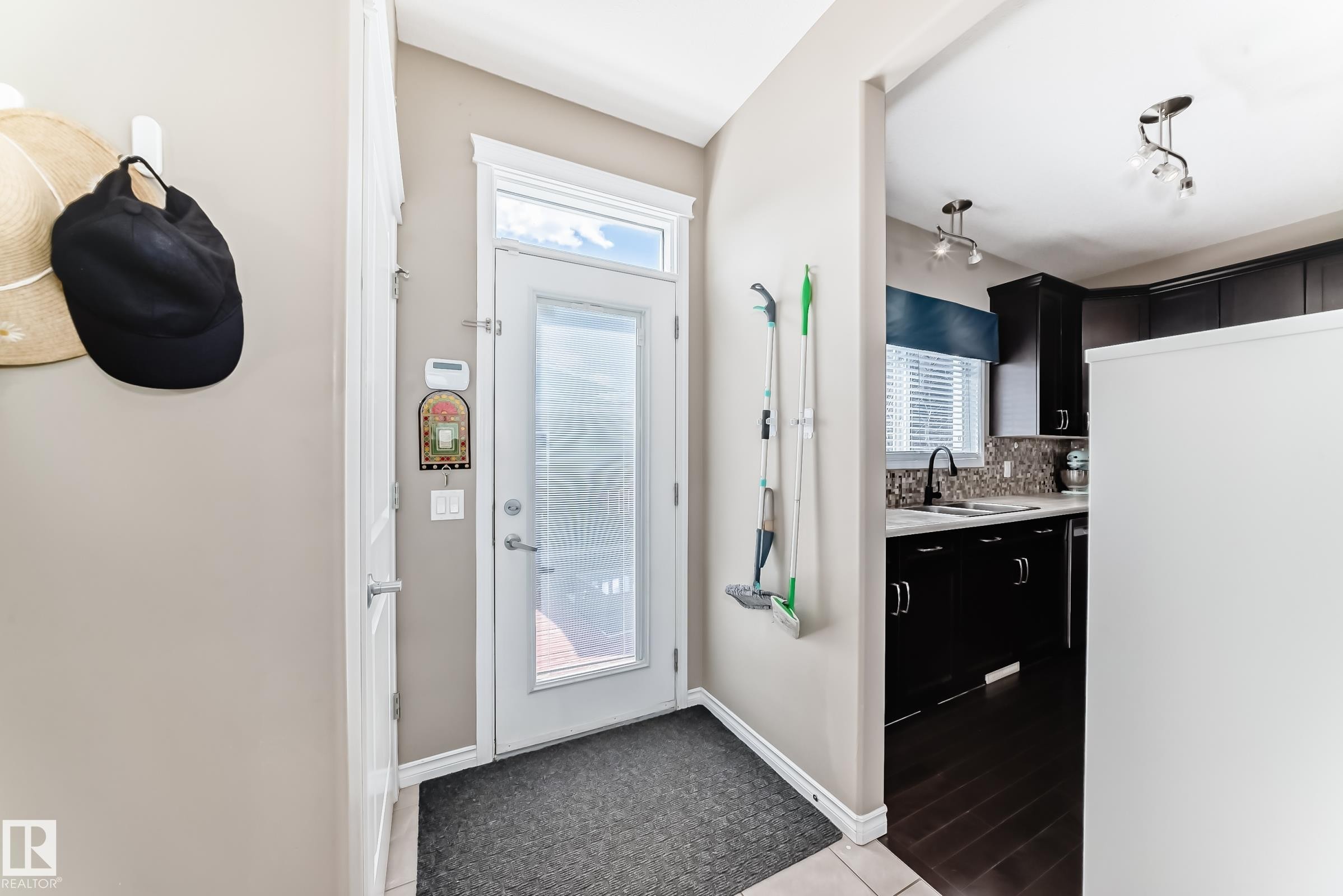 Entryway with a glass-paneled door and a kitchen featuring dark wood cabinetry, a tiled backsplash, a black faucet, and track lighting - 5020 Orchards Gate, Edmonton, AB - Indoor Photo Showing Other Room
