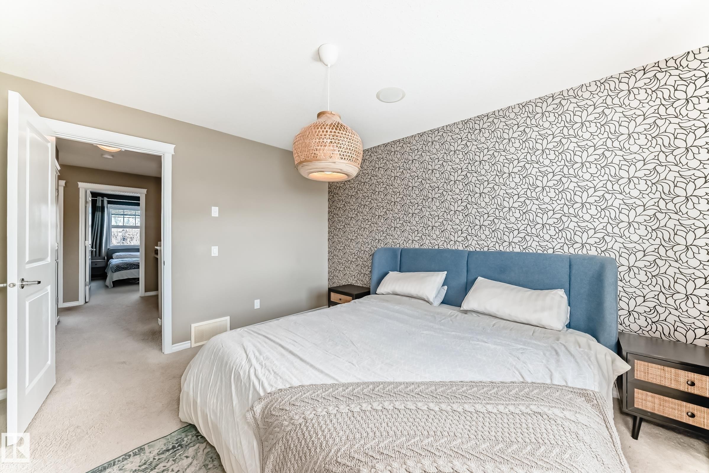 Bedroom featuring a patterned accent wall, plush carpeting, a modern pendant light fixture, and a built-in ceiling speaker - 5020 Orchards Gate, Edmonton, AB - Indoor Photo Showing Bedroom