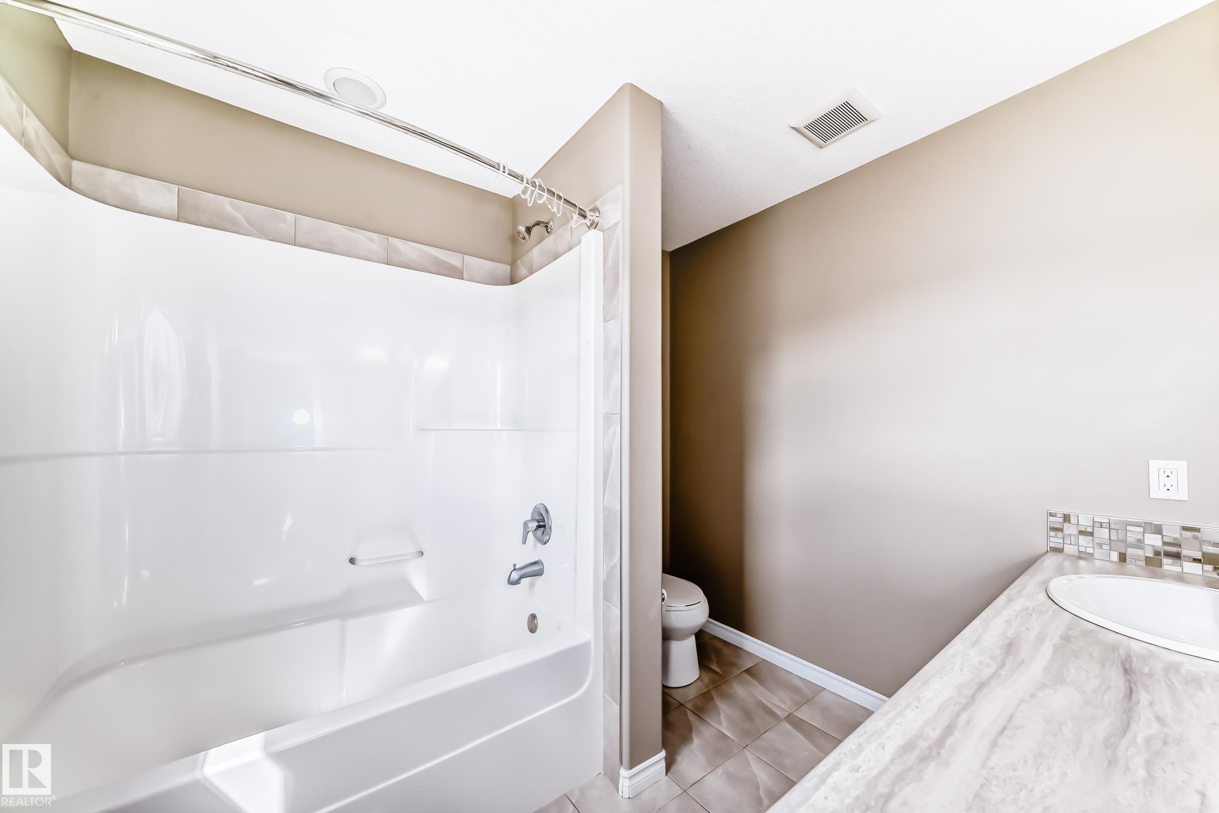 Bathroom featuring a white bathtub and shower combination, a single vanity with an integrated sink, a mosaic tile backsplash, and neutral wall paint - 5020 Orchards Gate, Edmonton, AB - Indoor Photo Showing Bathroom