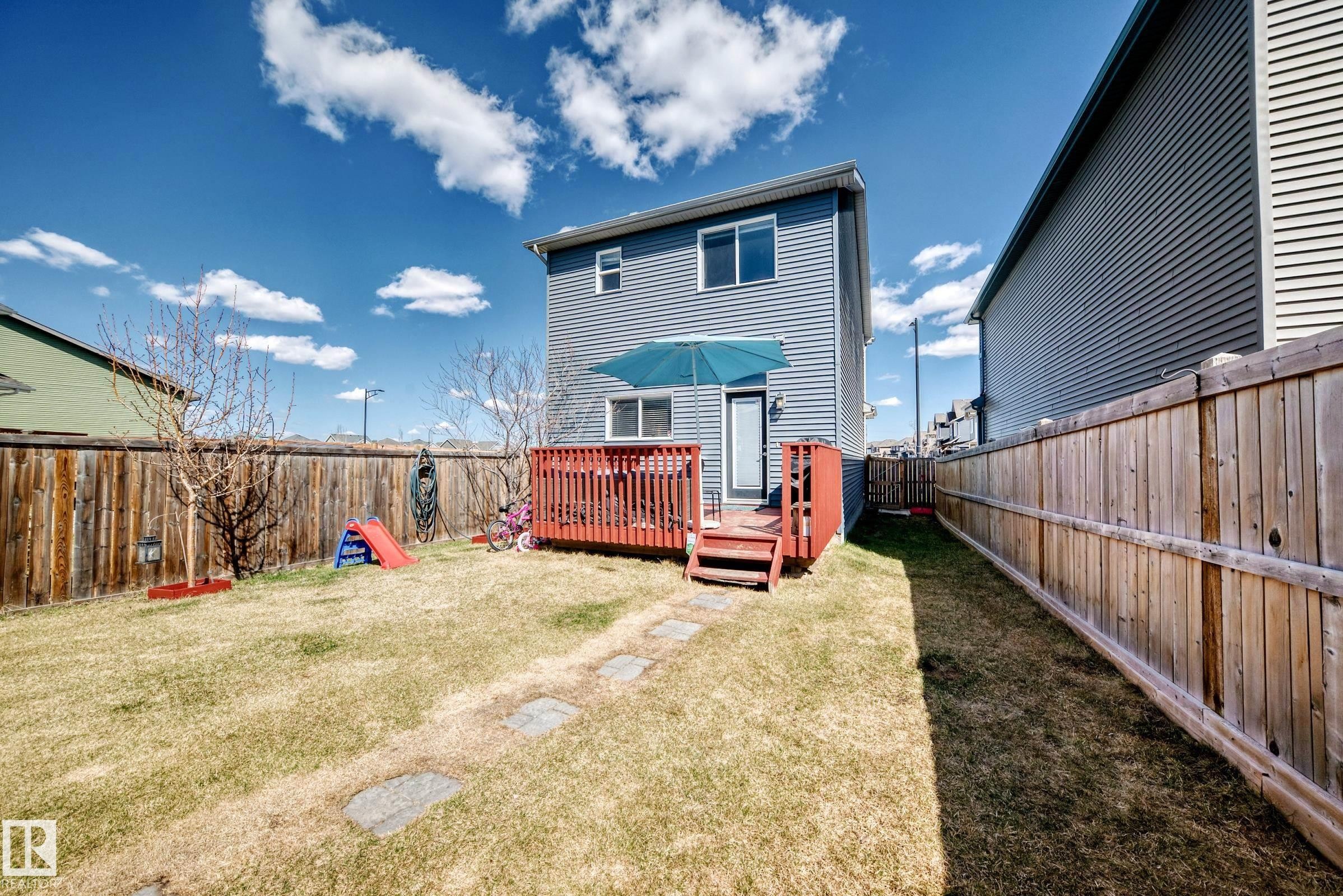 Rear exterior featuring blue horizontal siding, a red wood-finish deck with steps, and a glass-paneled door - 5020 Orchards Gate, Edmonton, AB - Outdoor With Deck Patio Veranda