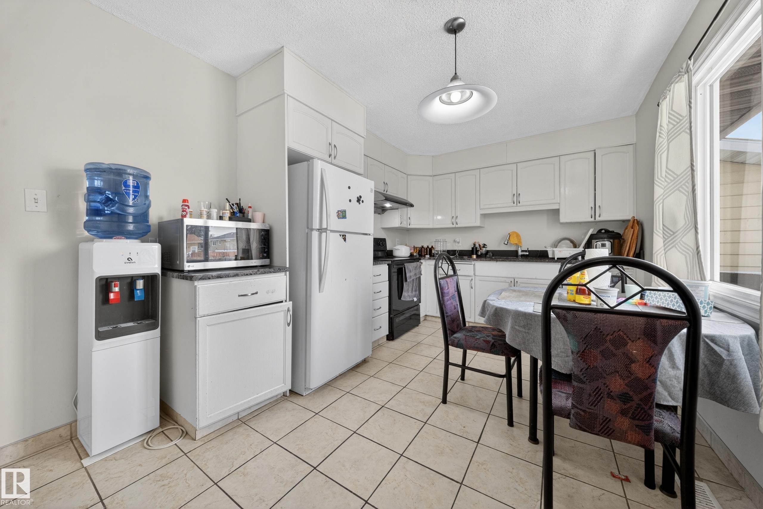 Kitchen featuring white cabinetry, light-toned tile flooring, and a large window - 8312 29 Ave Nw, Edmonton, AB - Indoor Photo Showing Other Room