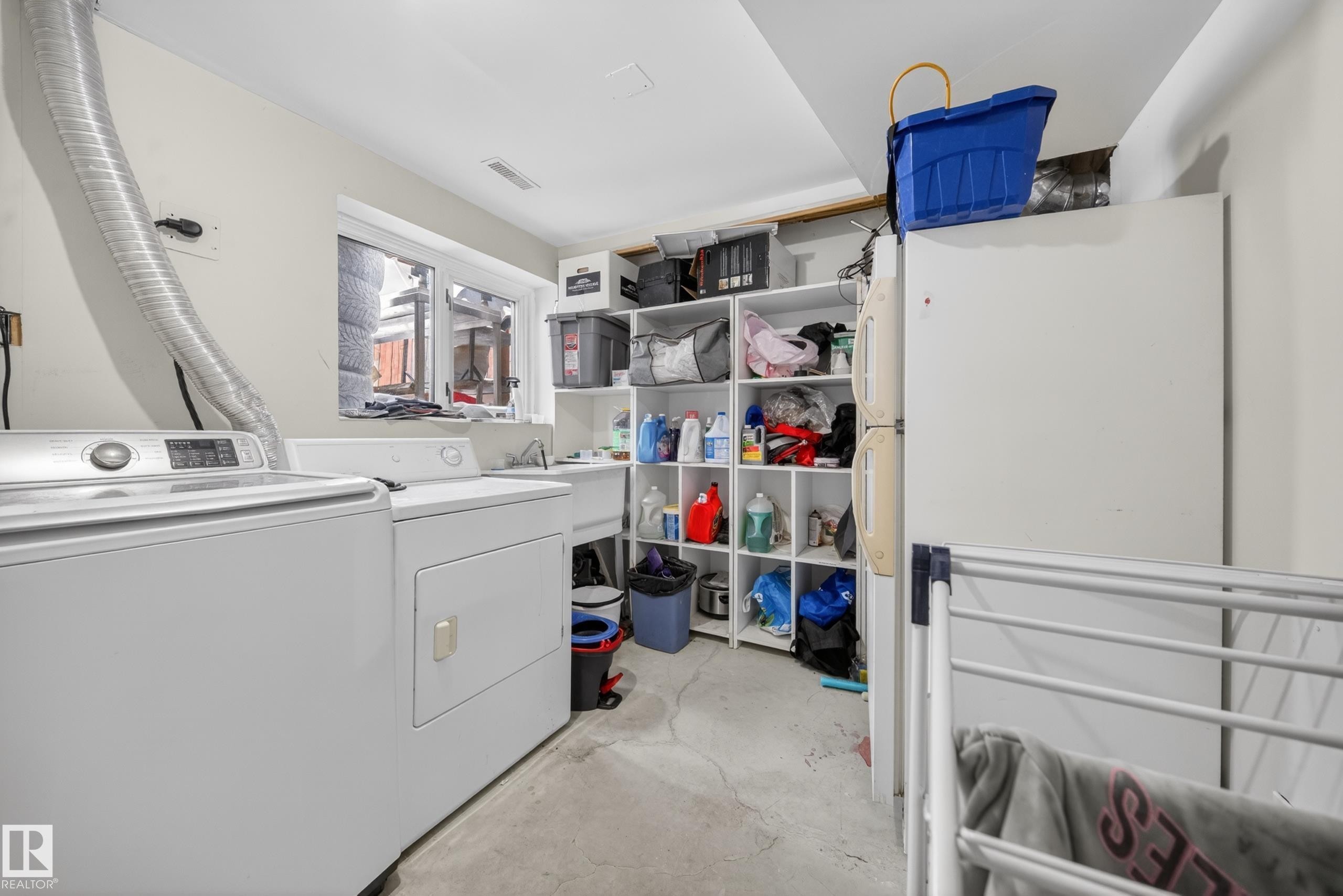 Dedicated laundry area featuring a window, built-in shelving, a utility sink, and concrete flooring - 8312 29 Ave Nw, Edmonton, AB - Indoor Photo Showing Laundry Room