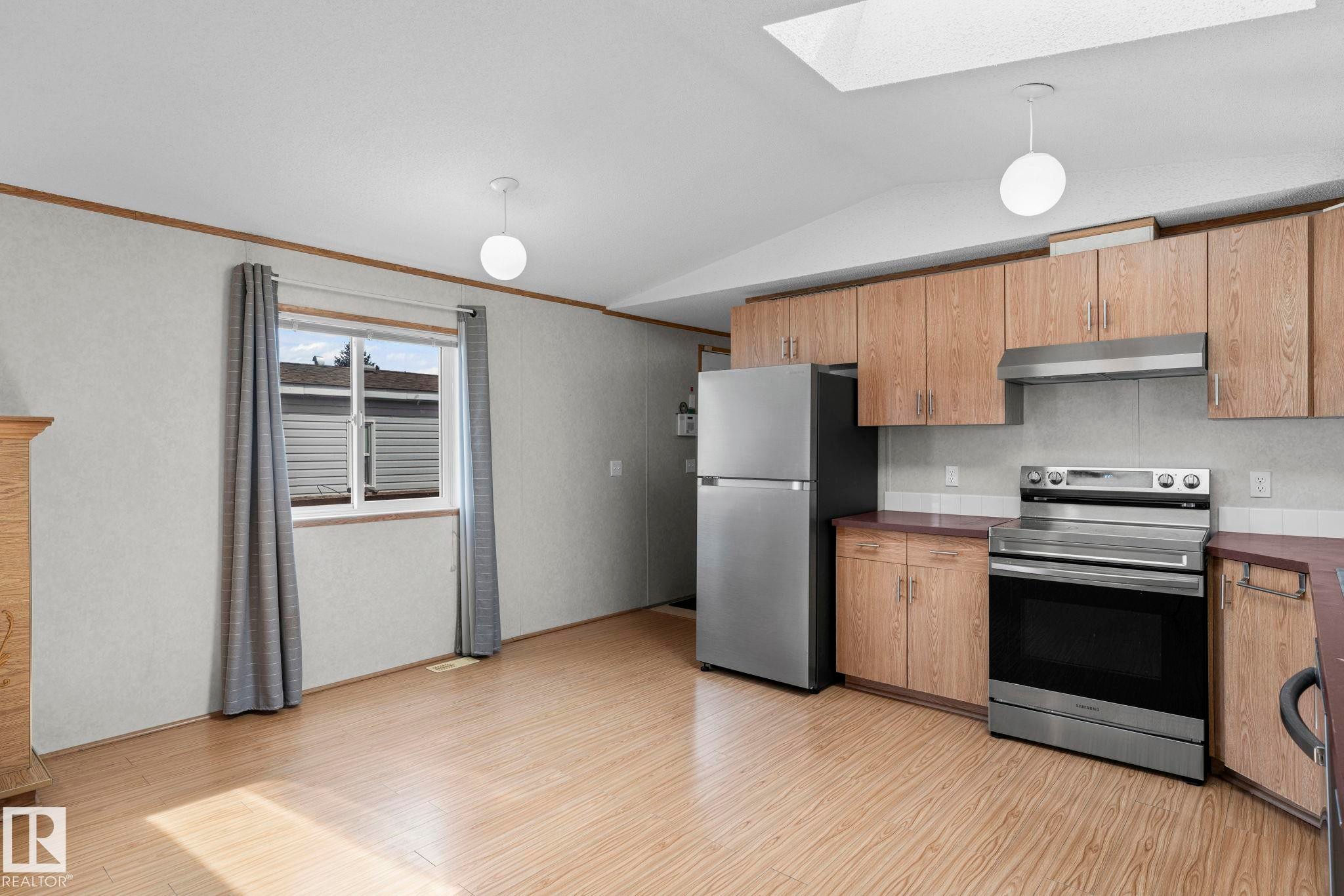Kitchen area featuring wood-finish flooring, light wood cabinetry, stainless steel appliances, a white ceiling, and a skylight - 623 Evergreen Park, Edmonton, AB - Indoor Photo Showing Kitchen