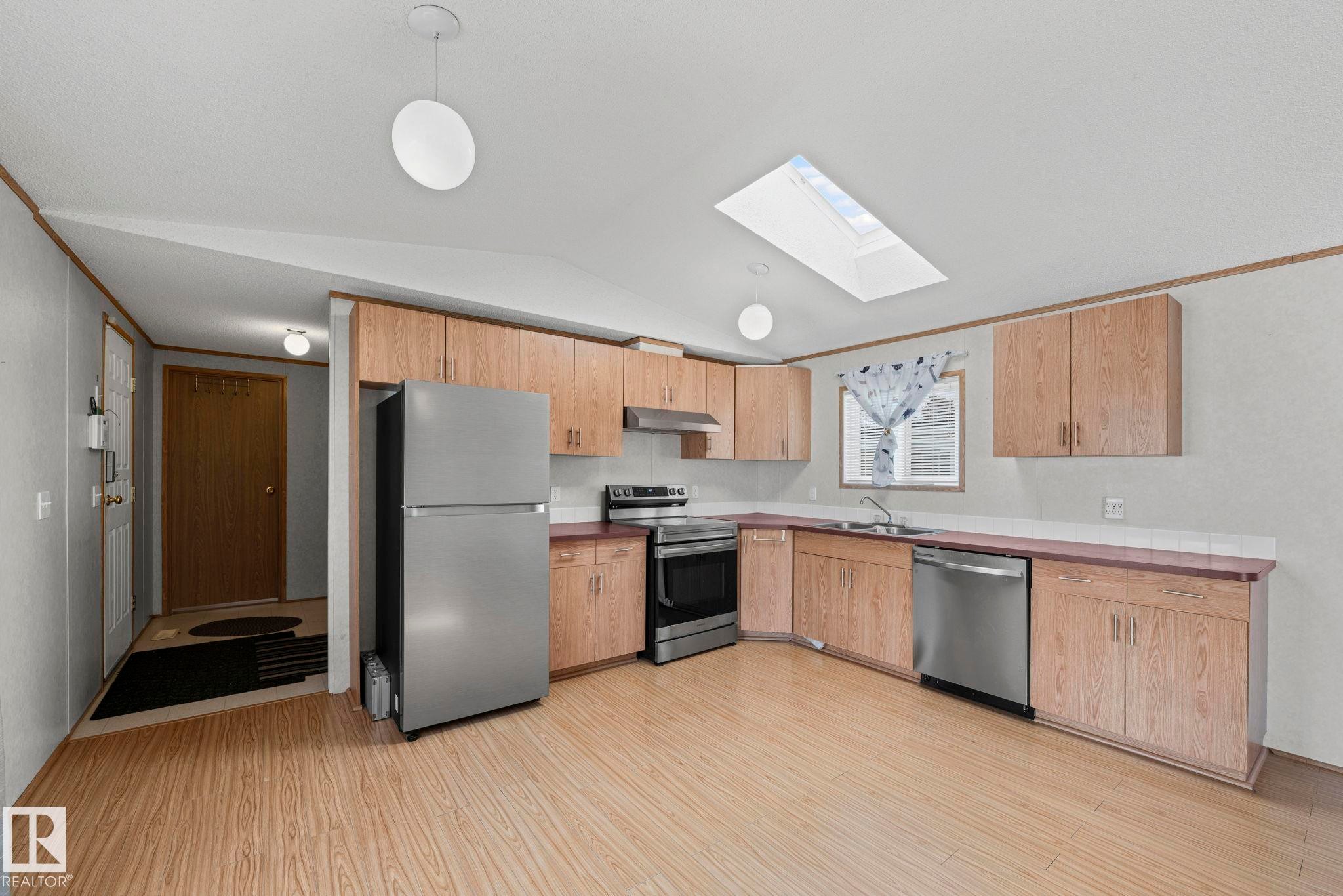 Kitchen featuring wood-finish flooring, light wood cabinetry, stainless steel appliances, and a skylight - 623 Evergreen Park, Edmonton, AB - Indoor Photo Showing Kitchen With Double Sink