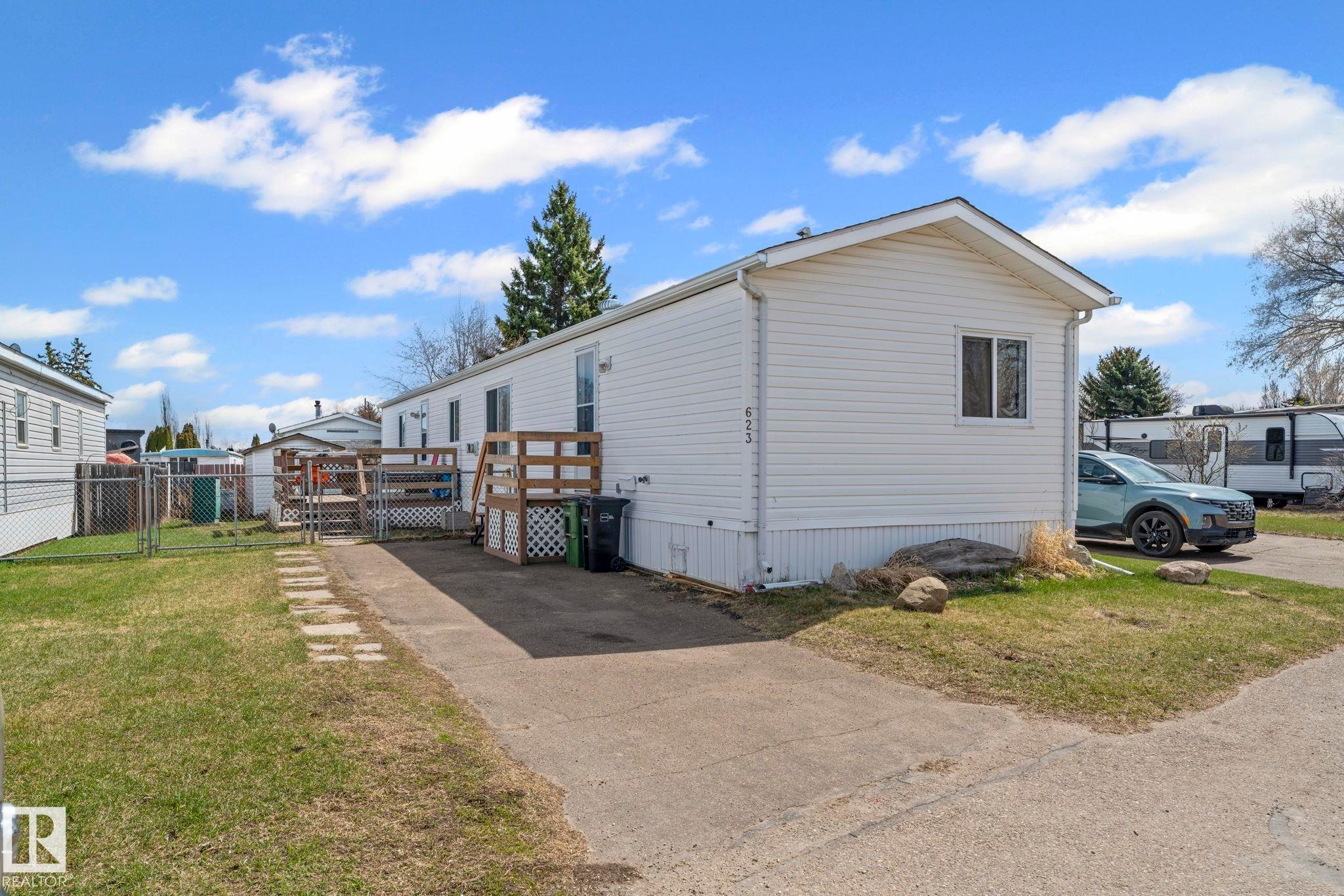 White siding exterior with a pitched roofline, concrete driveway, and a wood deck with lattice skirting - 623 Evergreen Park, Edmonton, AB - Outdoor