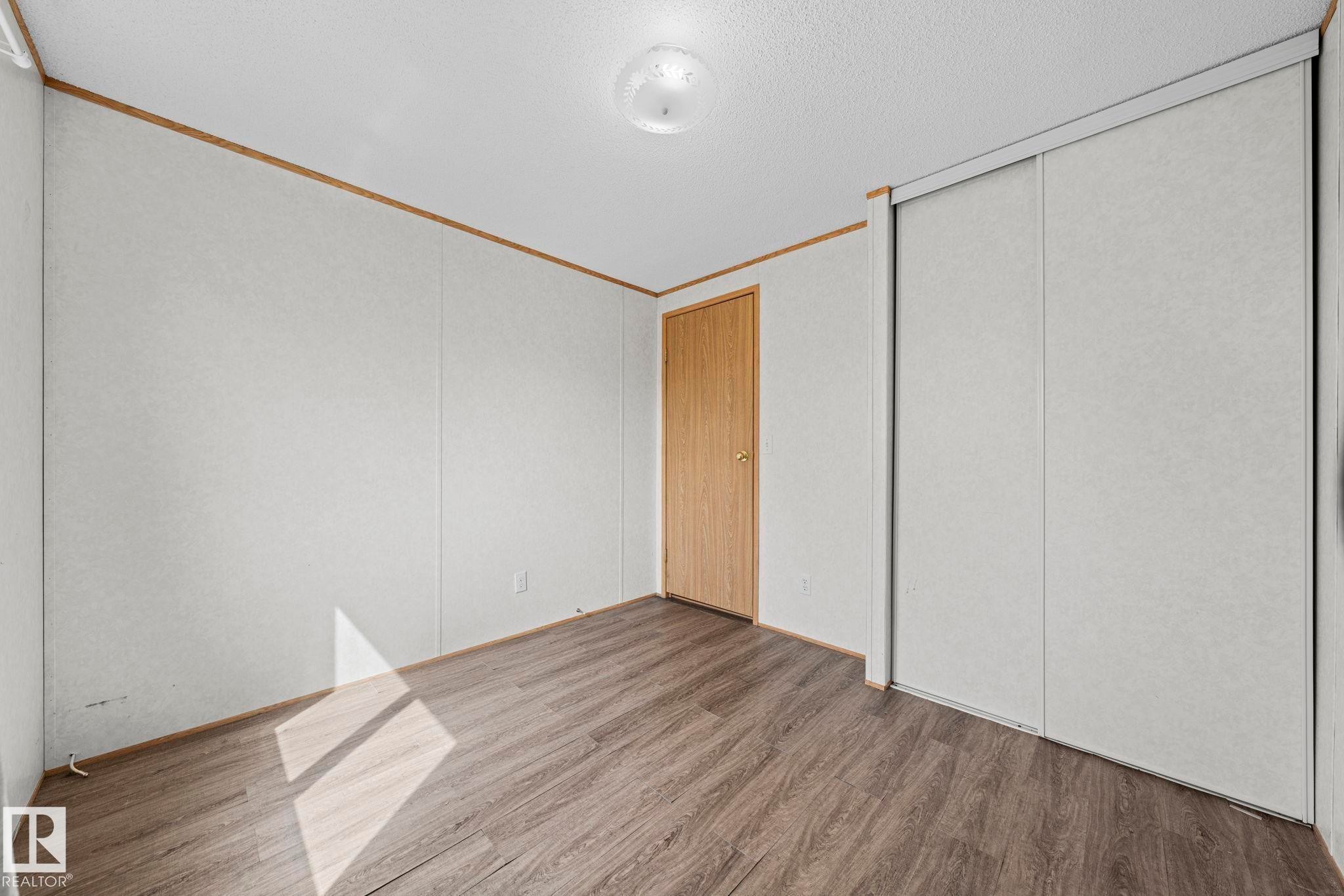 Room featuring wood-finish flooring, light-toned walls, a flush-mount ceiling light fixture, a light wood door, and a built-in sliding panel closet - 623 Evergreen Park, Edmonton, AB - Indoor Photo Showing Other Room