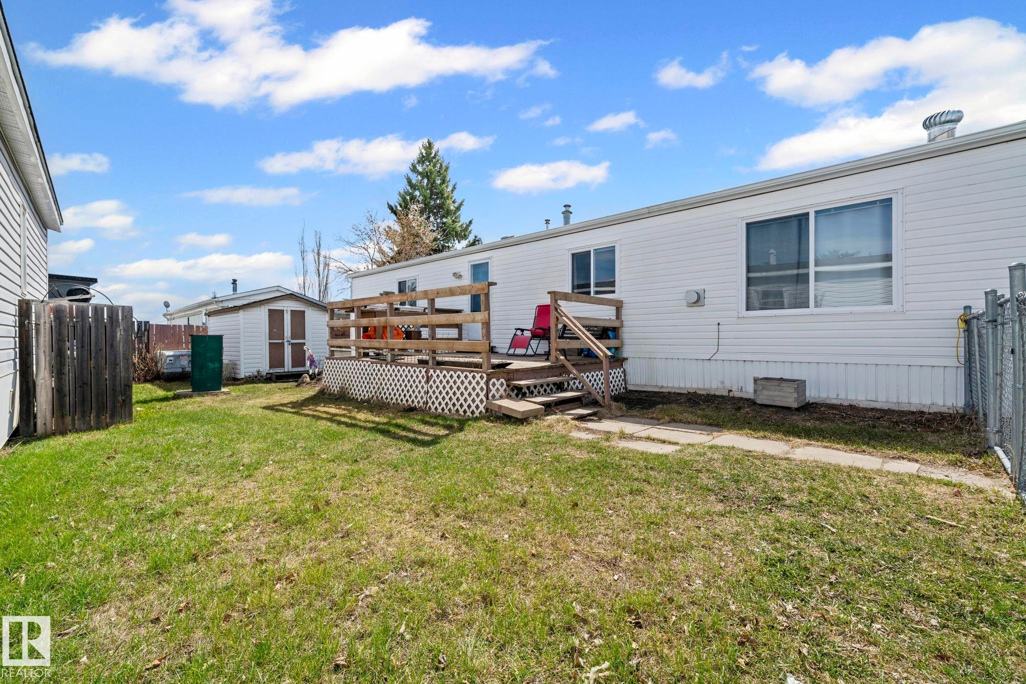 Rear exterior featuring white horizontal siding, a wooden deck with railing, a small outbuilding, and a chain-link fence - 623 Evergreen Park, Edmonton, AB - Outdoor With Exterior