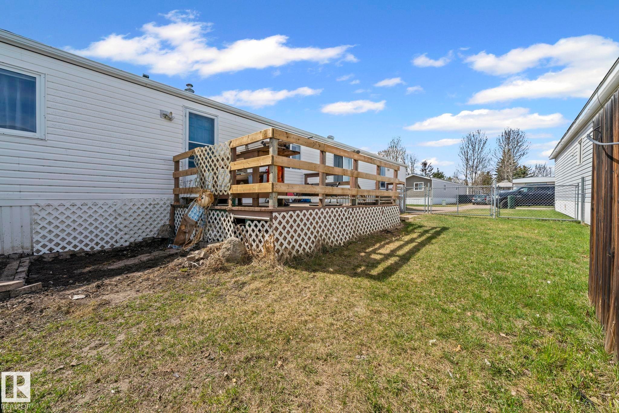 Rear exterior featuring a wood deck with wood railings, white lattice skirting, and a partial chain-link fence - 623 Evergreen Park, Edmonton, AB - Outdoor With Deck Patio Veranda
