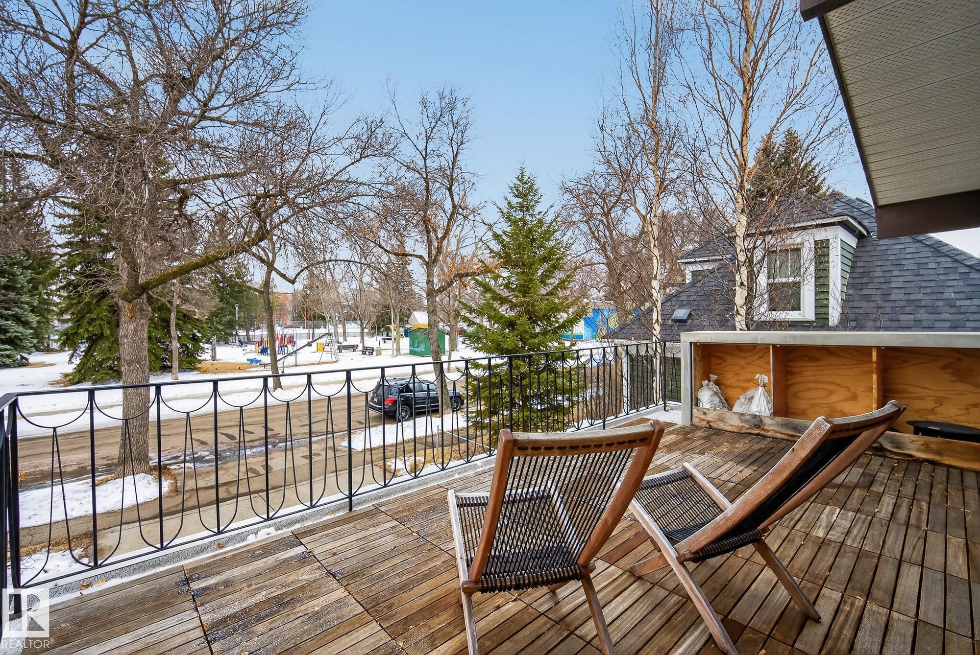 Expansive outdoor deck with a wooden surface and black metal railing, overlooking a park area with mature trees and snow-covered ground - 9736 78 Avenue, Edmonton, AB - Outdoor With Deck Patio Veranda With Exterior