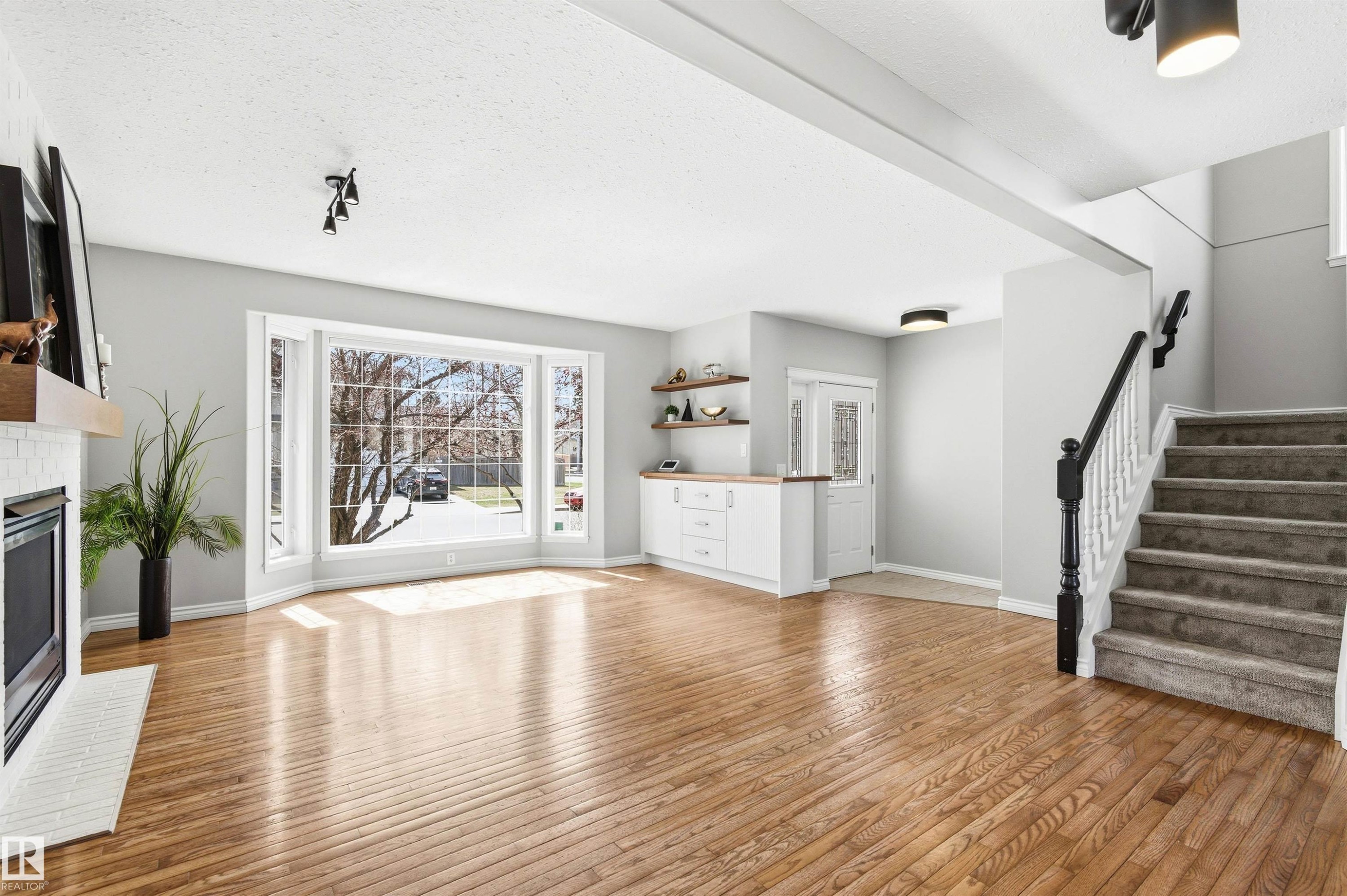 Spacious living area featuring polished wood-finish flooring, a white brick fireplace with a wood mantle, and a large bay window - 8730 92A Avenue, Edmonton, AB - Indoor Photo Showing Living Room