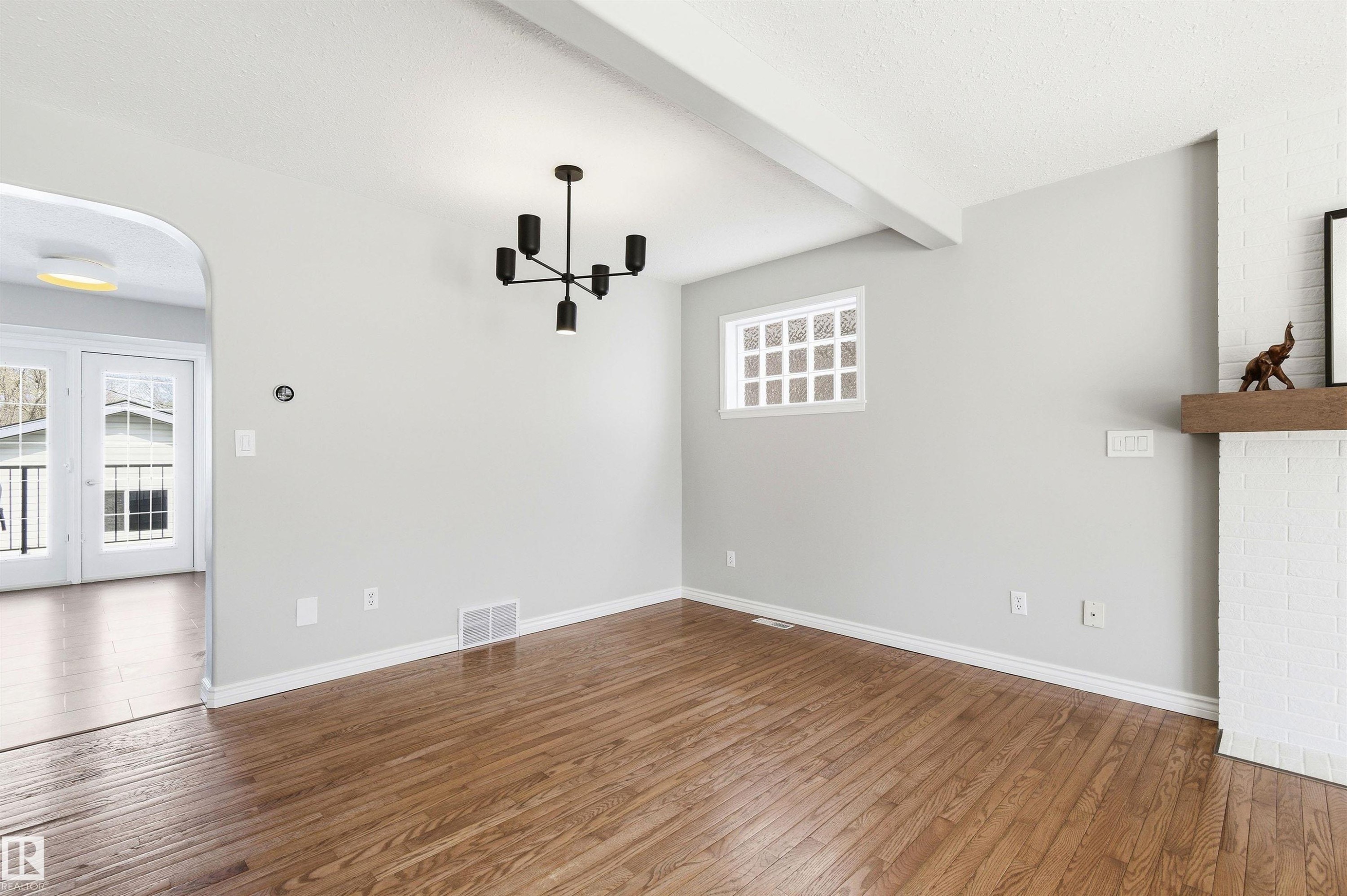 Hardwood flooring extending throughout, complemented by a white painted brick fireplace with a wood mantel - 8730 92A Avenue, Edmonton, AB - Indoor Photo Showing Other Room