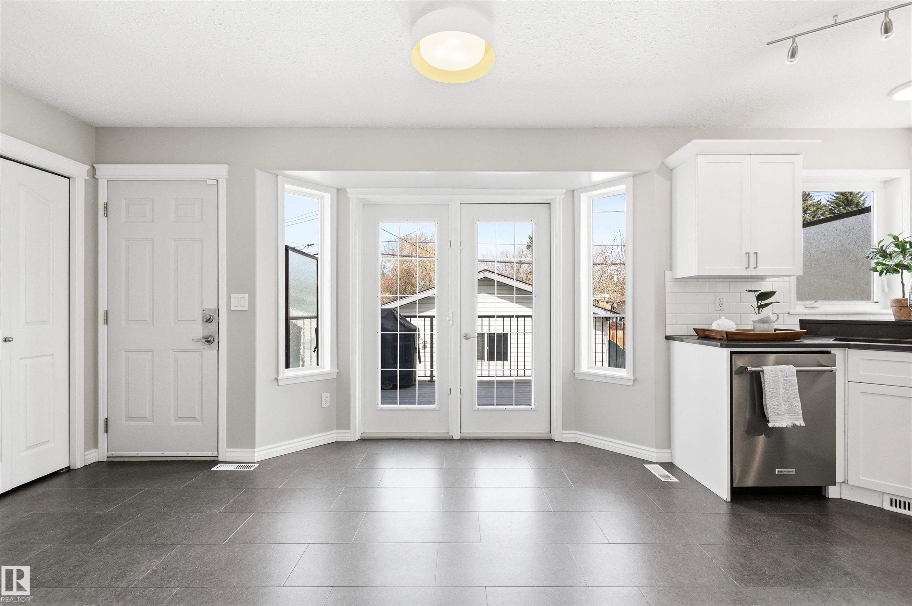 Open-concept space featuring dark tile flooring, white shaker-style cabinetry, and a stainless steel dishwasher - 8730 92A Avenue, Edmonton, AB - Indoor Photo Showing Kitchen