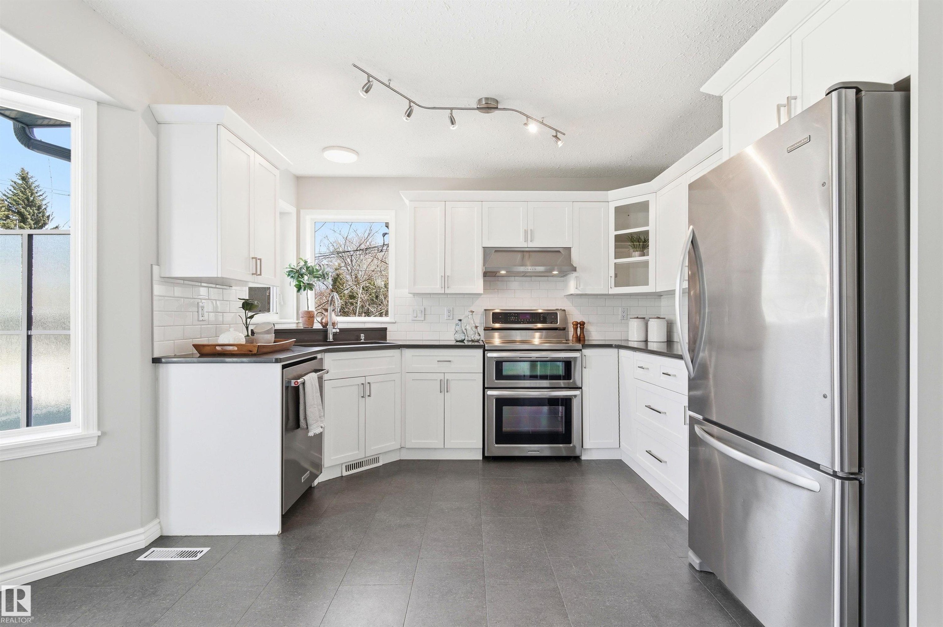 Bright kitchen featuring white cabinetry, dark countertops, and stainless steel appliances - 8730 92A Avenue, Edmonton, AB - Indoor Photo Showing Kitchen With Upgraded Kitchen