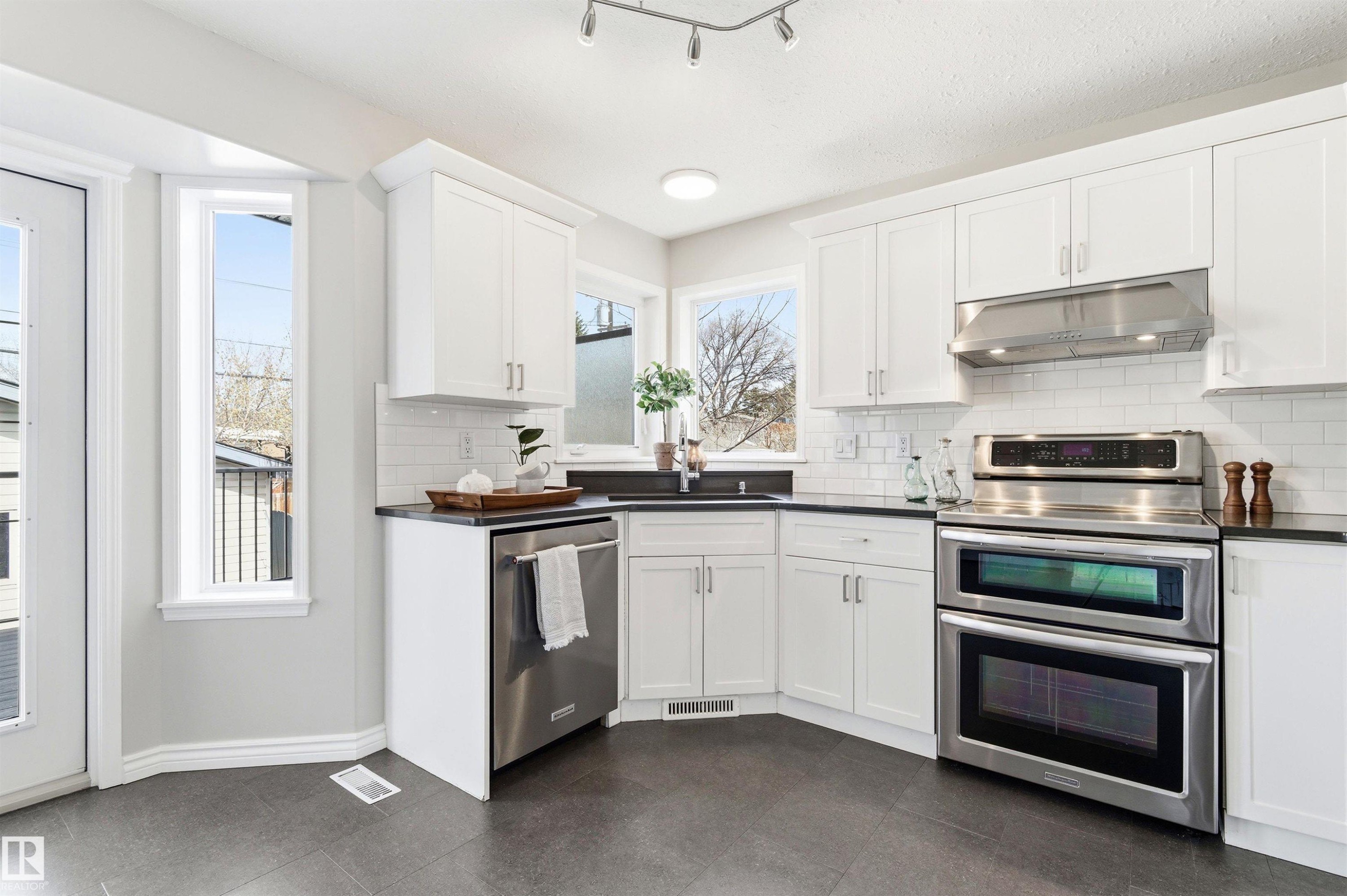Modern kitchen featuring white shaker cabinetry, dark countertops, a stainless steel double oven range, stainless steel dishwasher, and subway tile backsplash - 8730 92A Avenue, Edmonton, AB - Indoor Photo Showing Kitchen