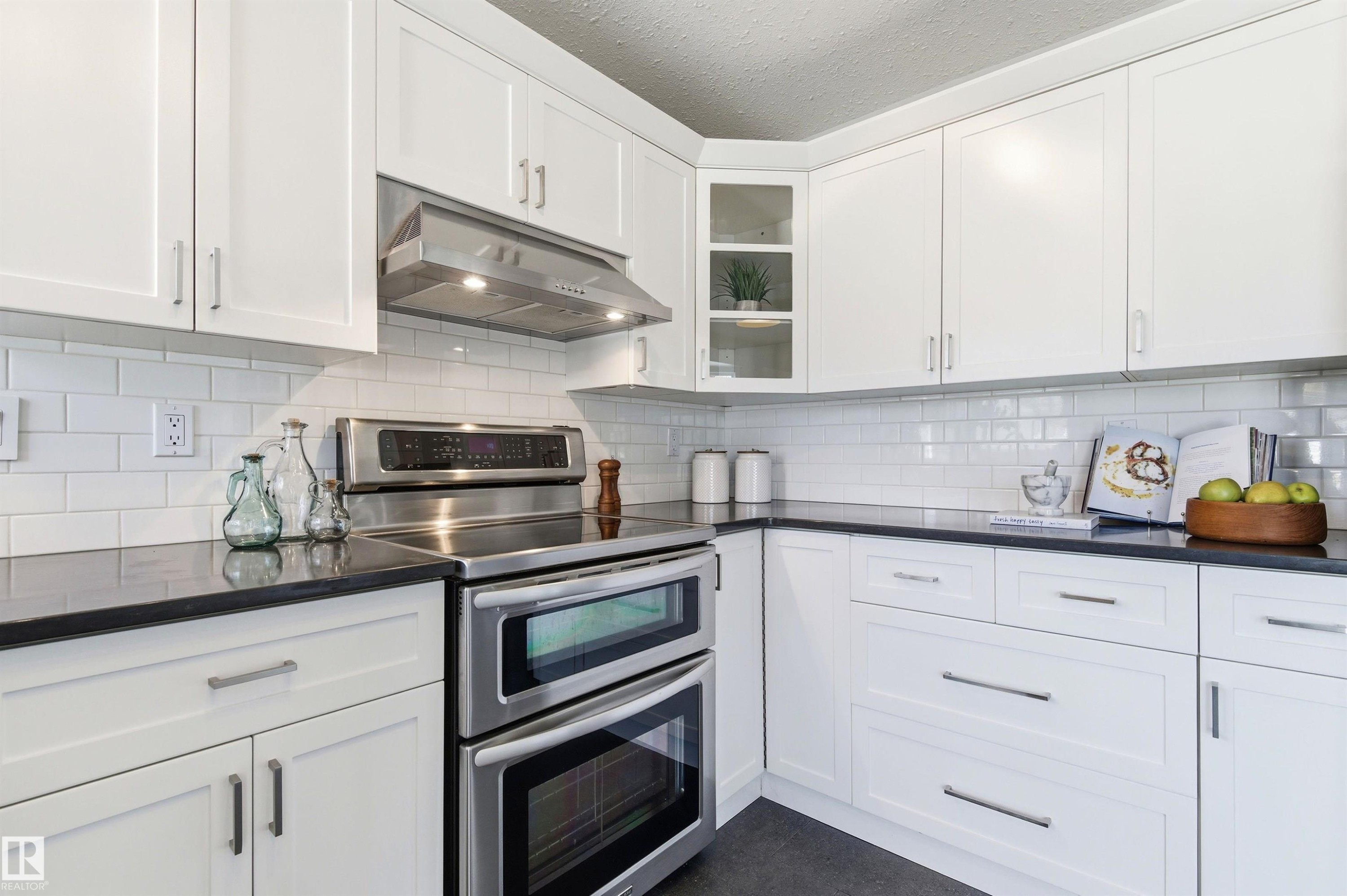 Modern kitchen featuring white shaker cabinetry, dark countertops, white subway tile backsplash, stainless steel double oven, and a stainless steel range hood - 8730 92A Avenue, Edmonton, AB - Indoor Photo Showing Kitchen