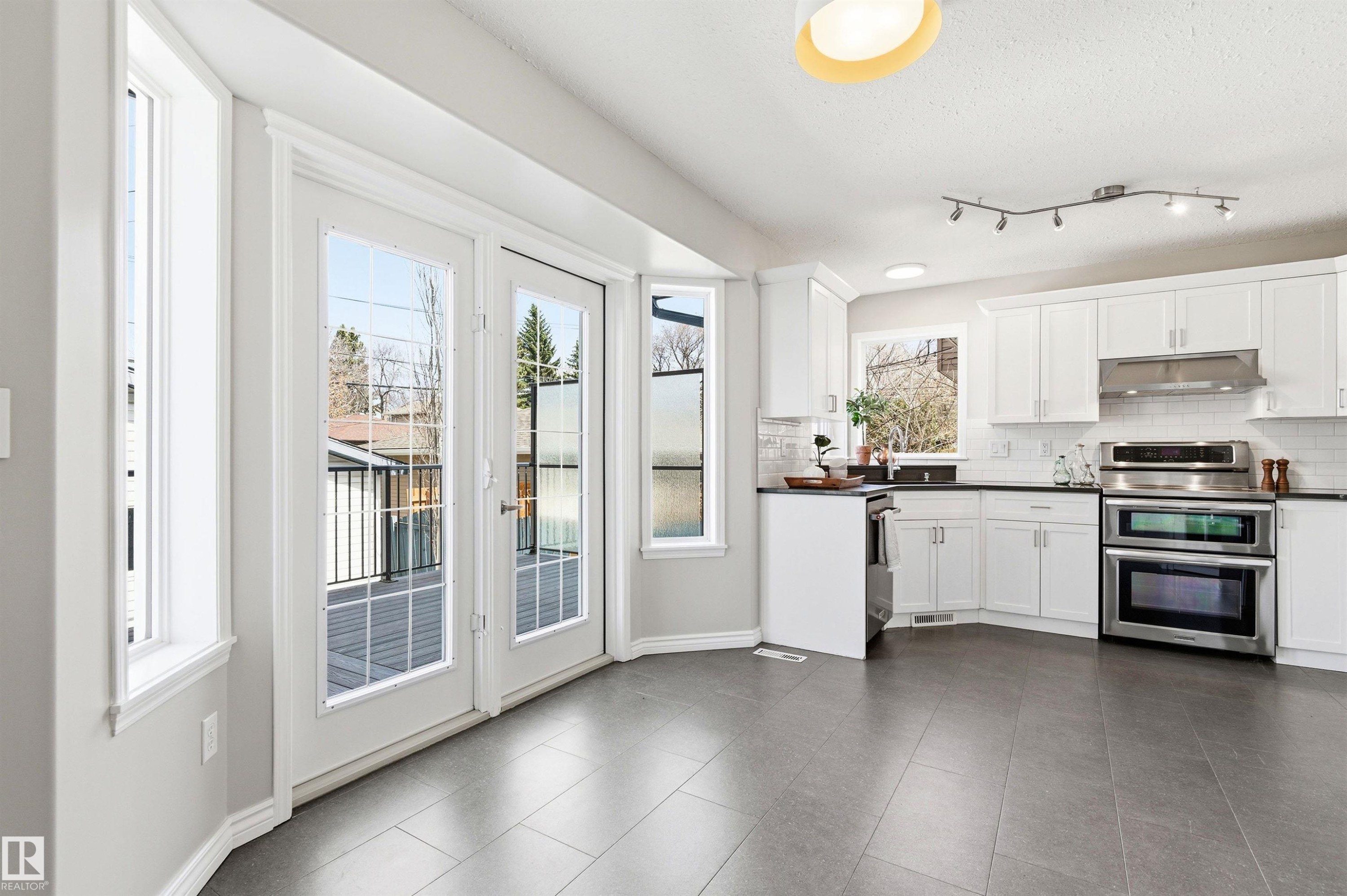 Open concept kitchen featuring white cabinetry, dark countertops, stainless steel appliances, a tile backsplash, and grey tile flooring - 8730 92A Avenue, Edmonton, AB - Indoor Photo Showing Kitchen With Upgraded Kitchen